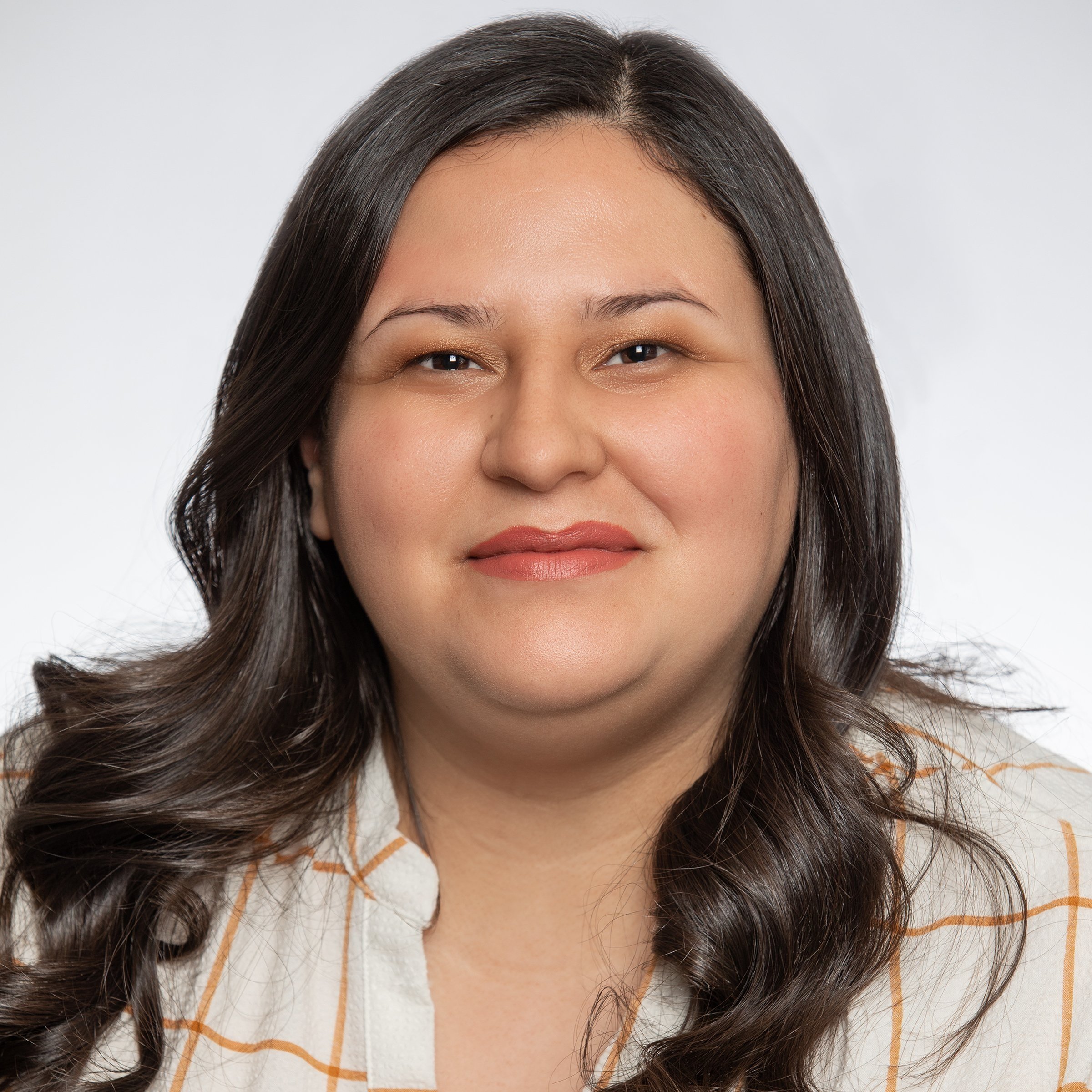A woman with wavy dark brown hair  with a white shirt with orange stripes.