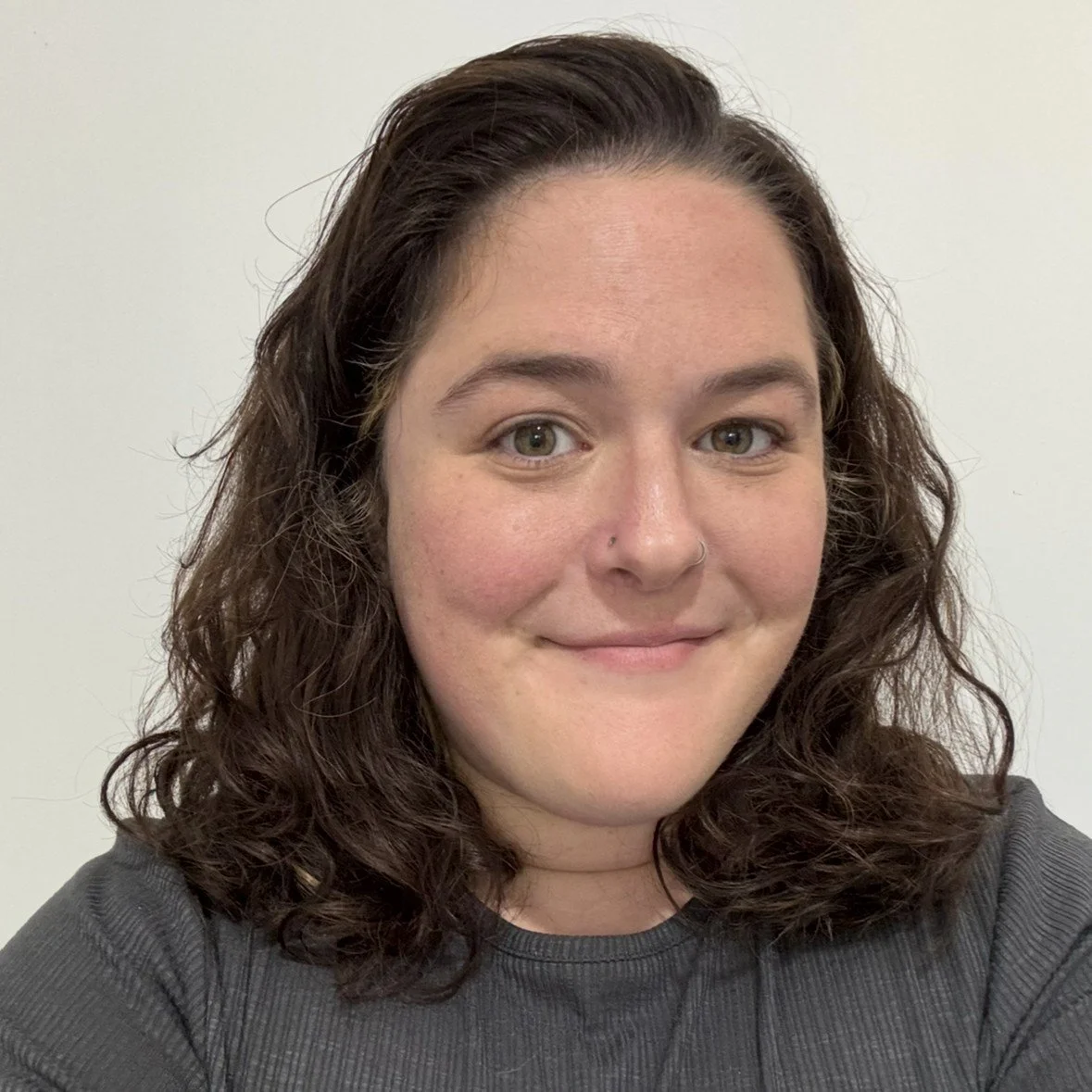 Smiling woman with long wavy brown hair wearing a grey blouse.