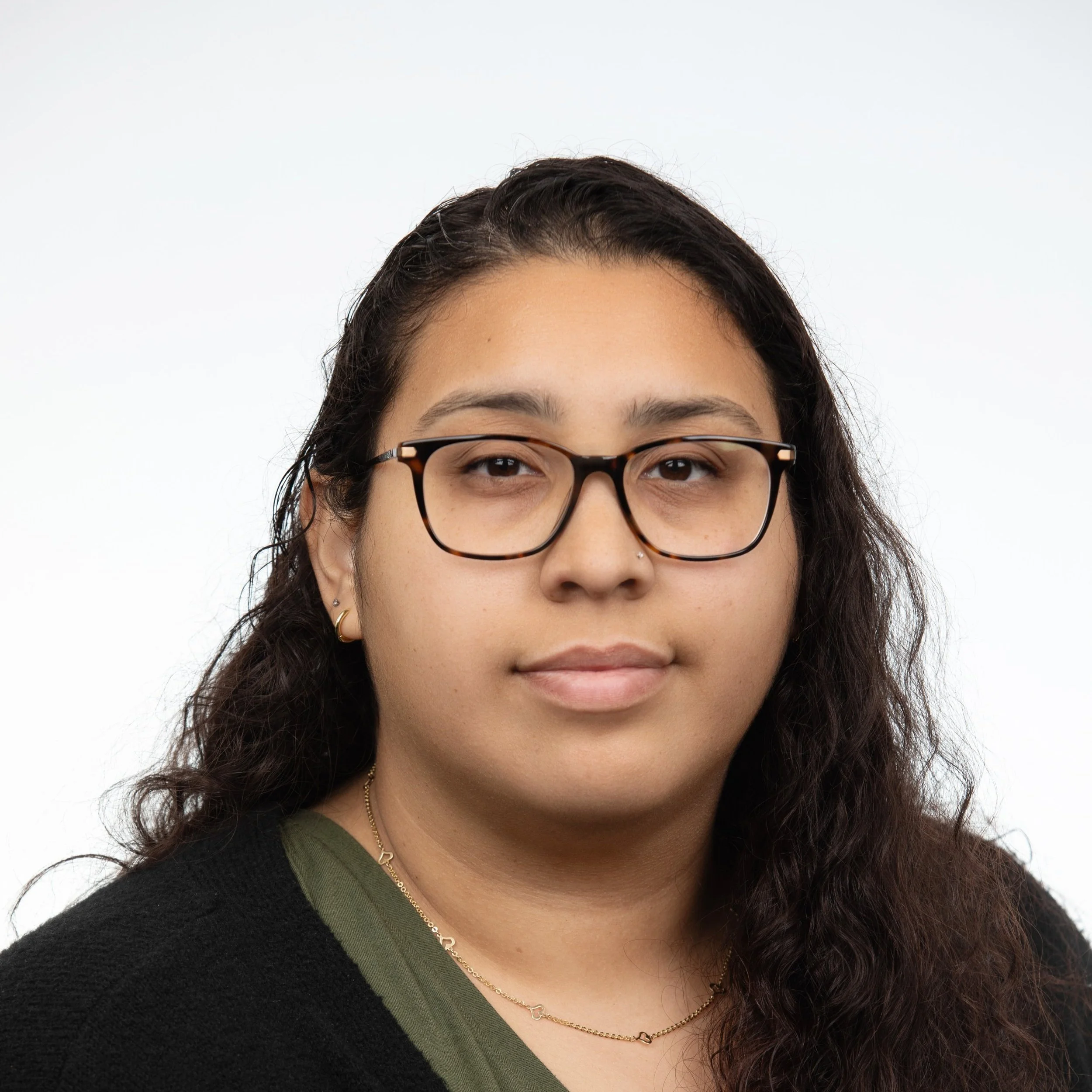 A woman with curly dark hair wearing glasses a green shirt with a black cardigan.