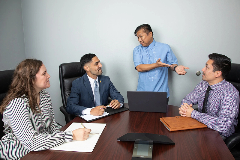 Man in blue collared shirt discusses business with two men and a woman.