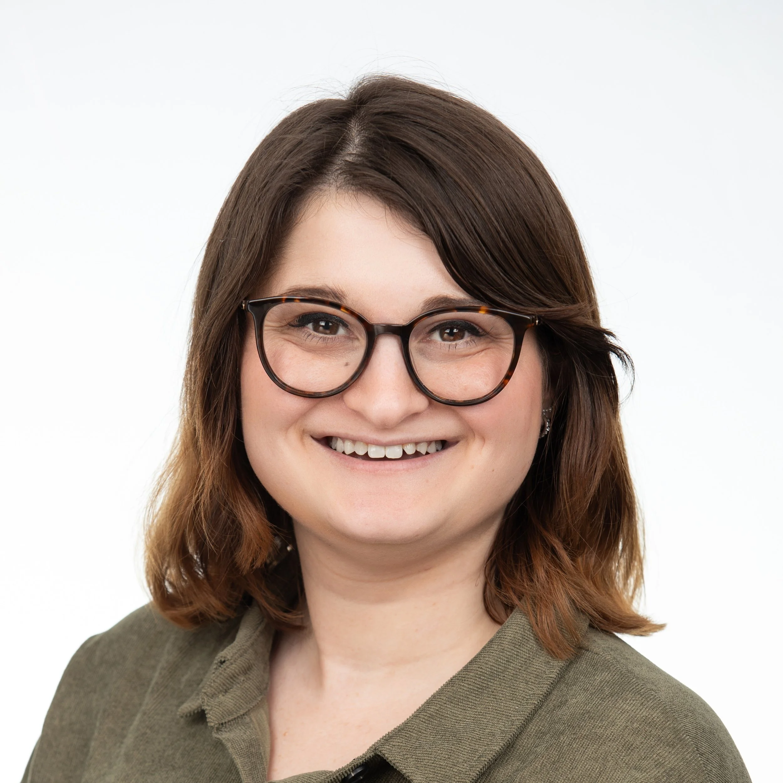 A woman smiling with short brown hair wearing glasses with an olive green collared shirt.