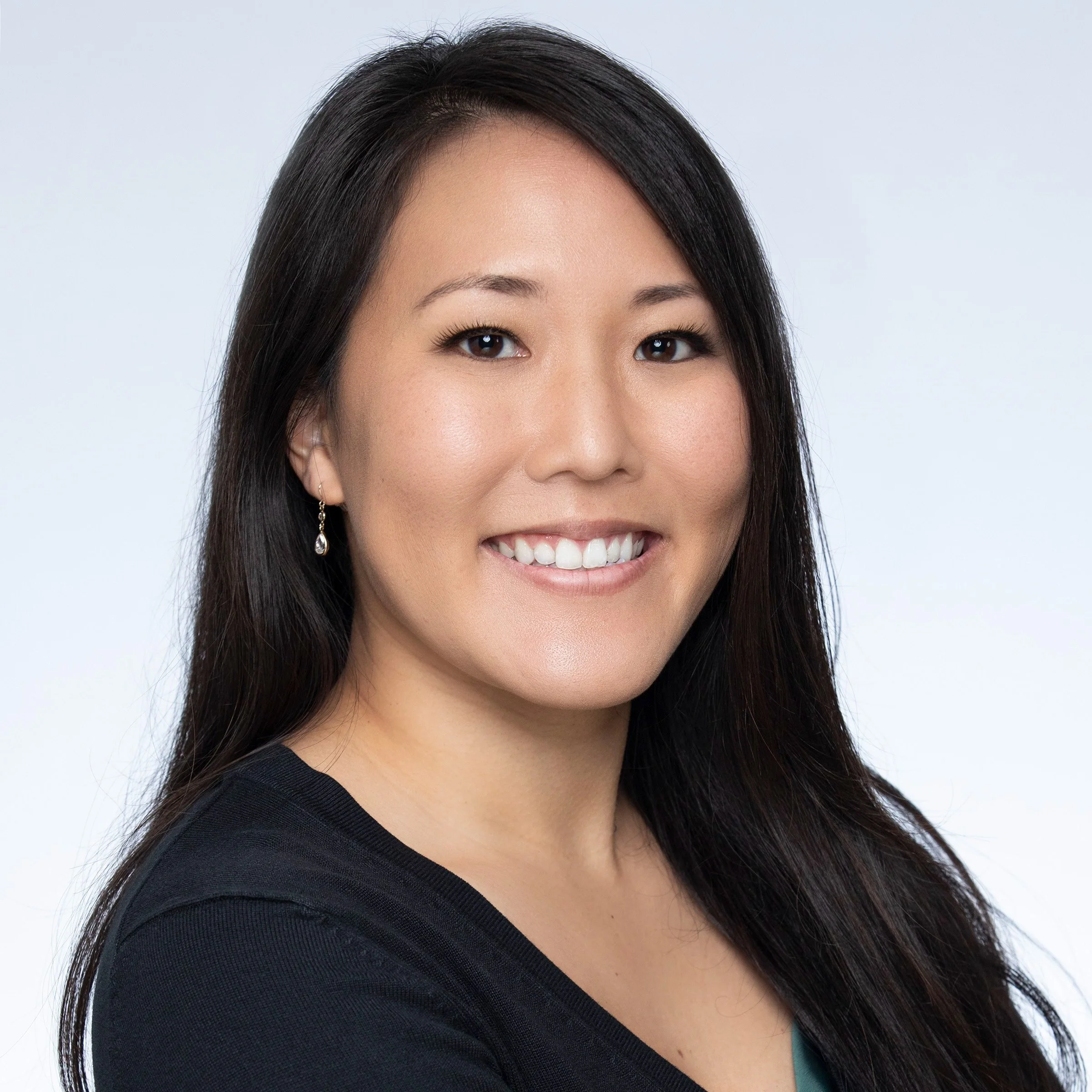 A woman smiling with long black hair wearing a black top.