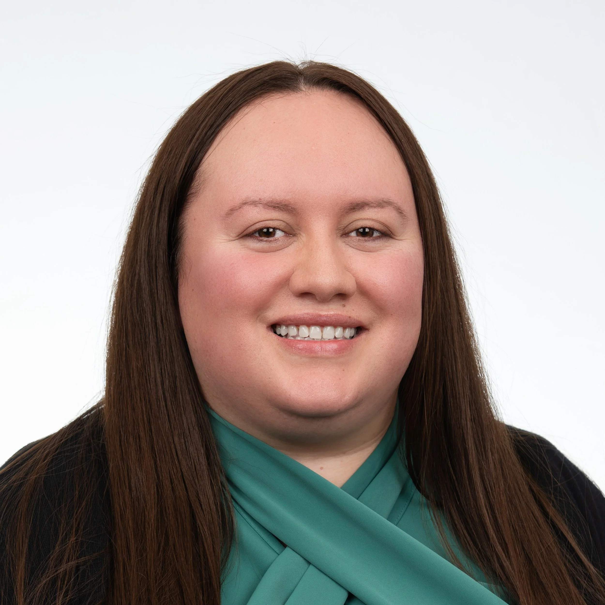A woman smiling with long brown hair wearing a emerald green top with a black cardigan.