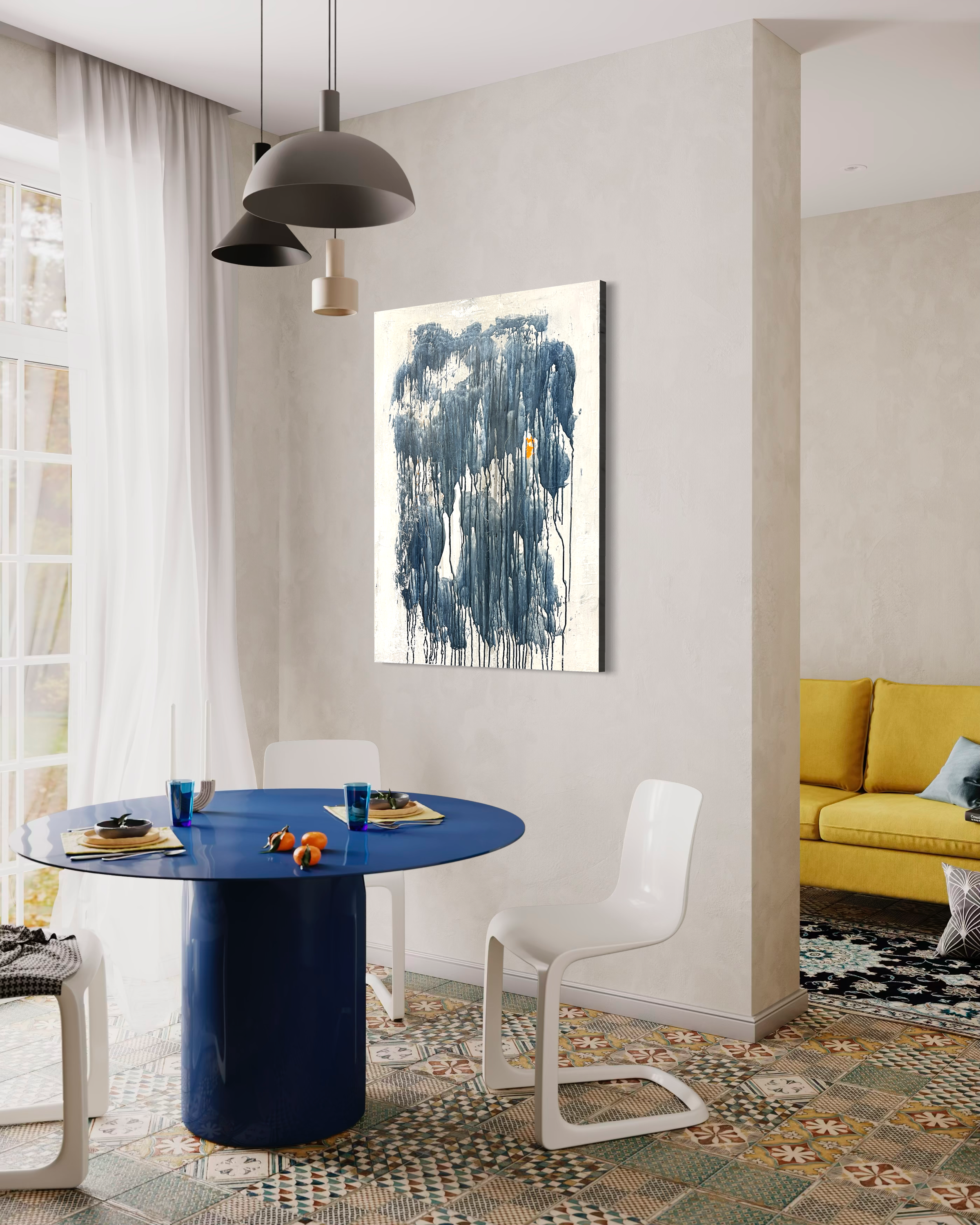Dining area with a round blue table set with plates, glasses, and small decorative items, surrounded by white chairs, with artwork on the wall and a yellow sofa in the background, and colorful patterned tile flooring.