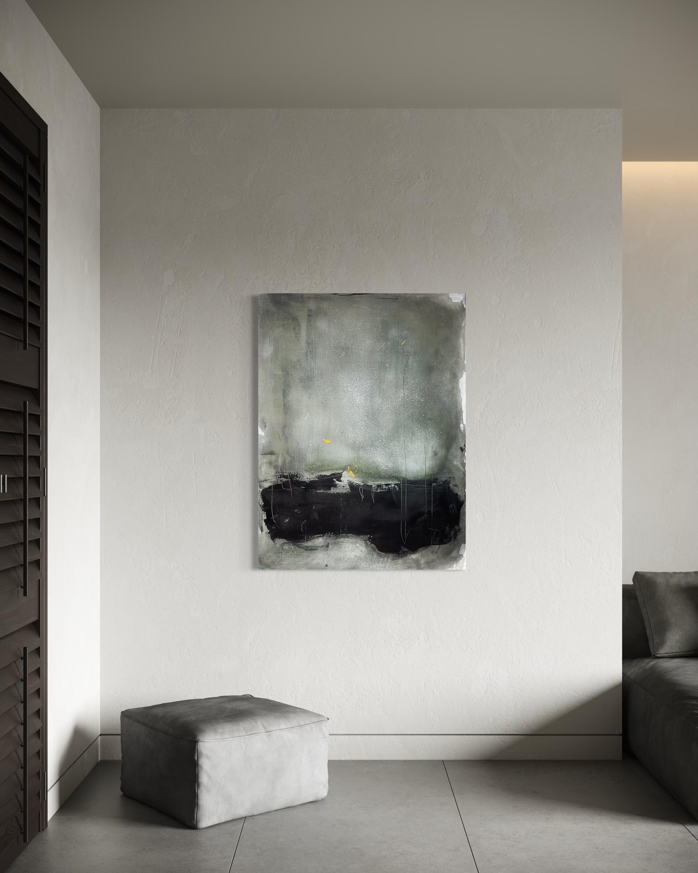 Minimalist gray living room wall with abstract painting, gray ottoman, and gray sofa visible on the right.