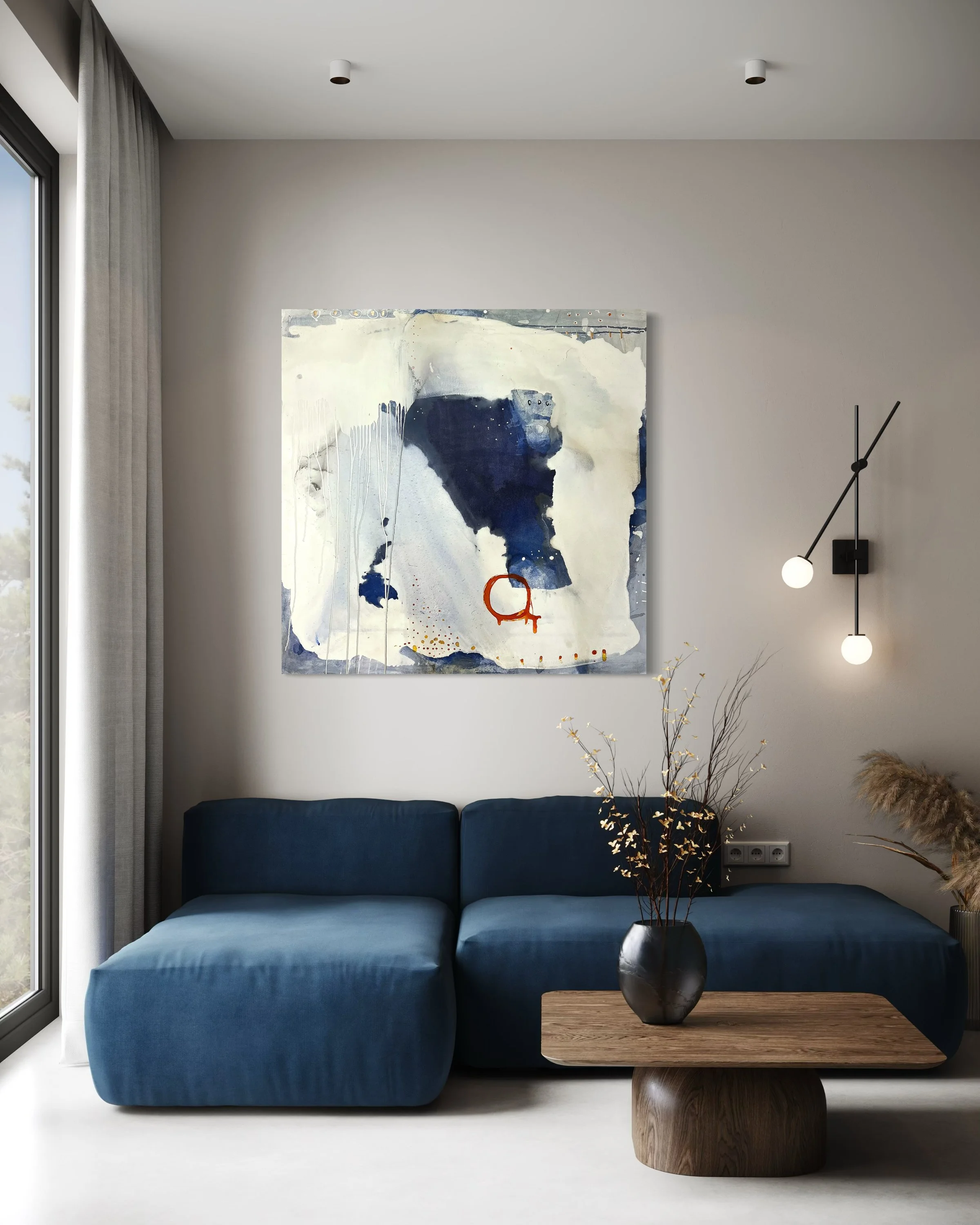 Living room with grey wall art, blue sofa, wooden coffee table, large window with curtains, side lamps, and decorative branches in a vase.