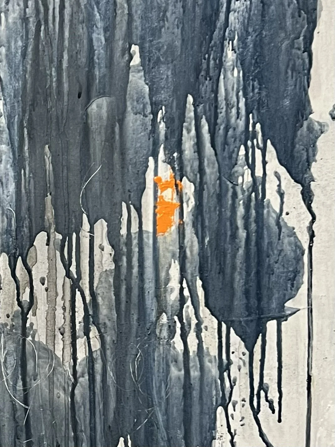 Close-up of an abstract painting featuring dark vertical streaks and drips with a small bright orange patch in the center.