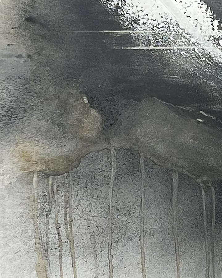 Graffiti of a face painted on a wet, dirty wall with water streaks running down.