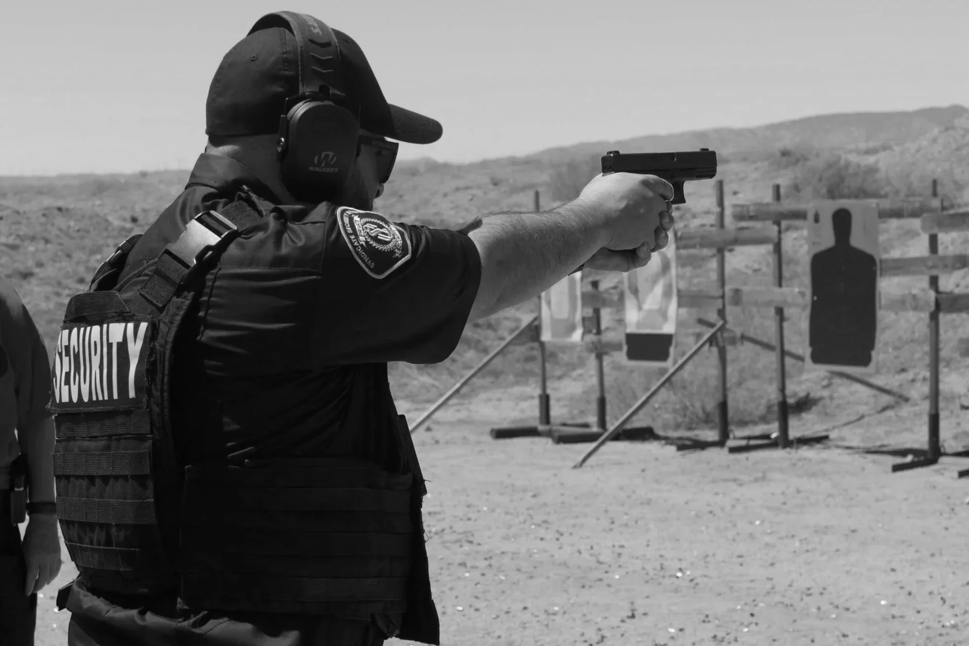 A security officer firing a handgun at a shooting range with target silhouettes in the background.