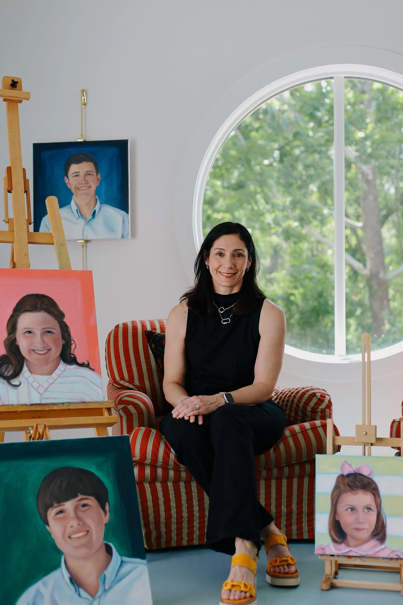 Artist Libbie Patterson in her studio surrounded by custom acrylic child portrait commissions, showcasing her portrait painting process and original artwork.
