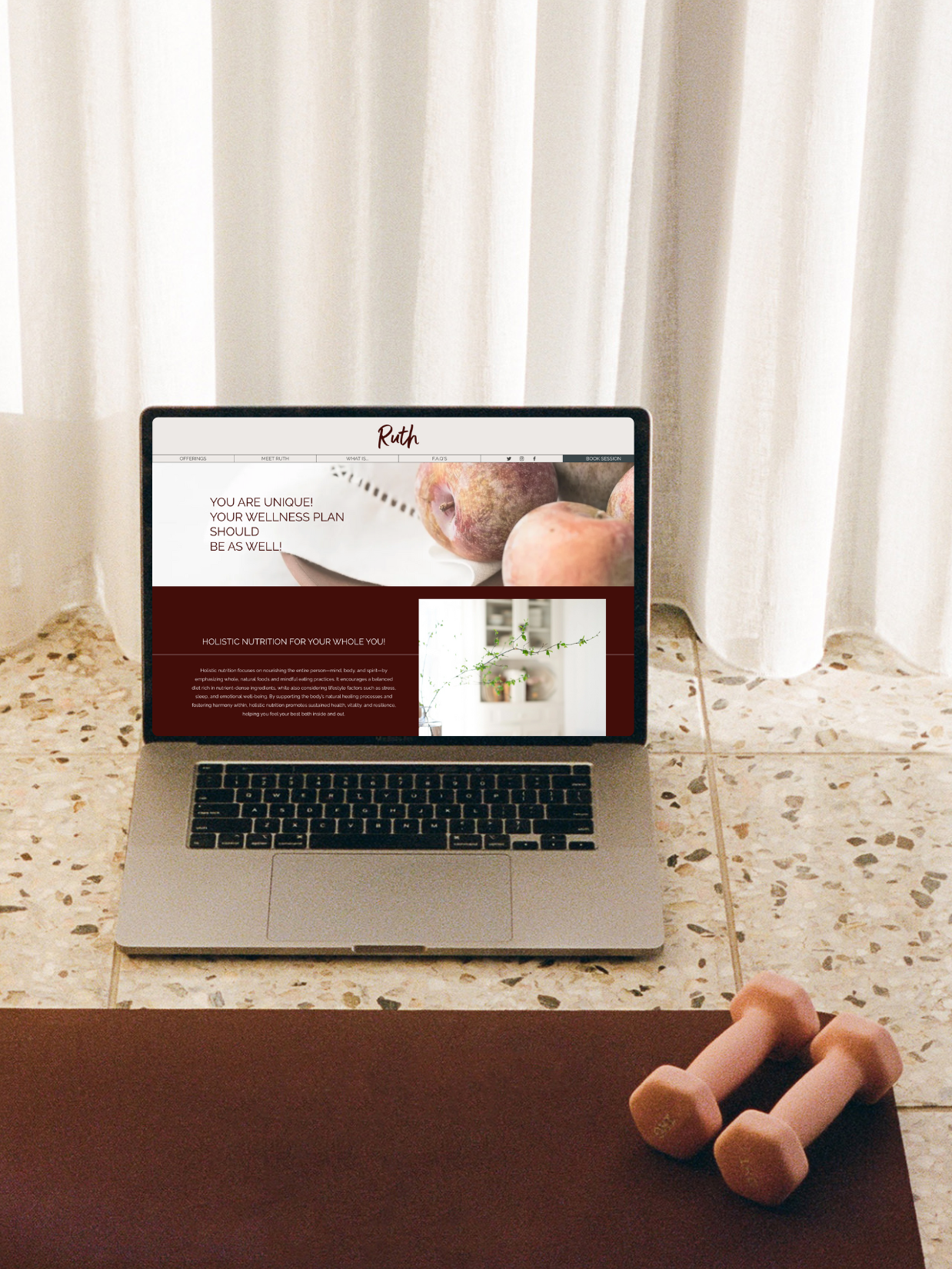 A laptop on a tiled floor displays a website about holistic nutrition, with a section titled 'You are unique! Your wellness plan should be as well!' In front of the laptop, a small pair of pink dumbbells is on a brown mat.