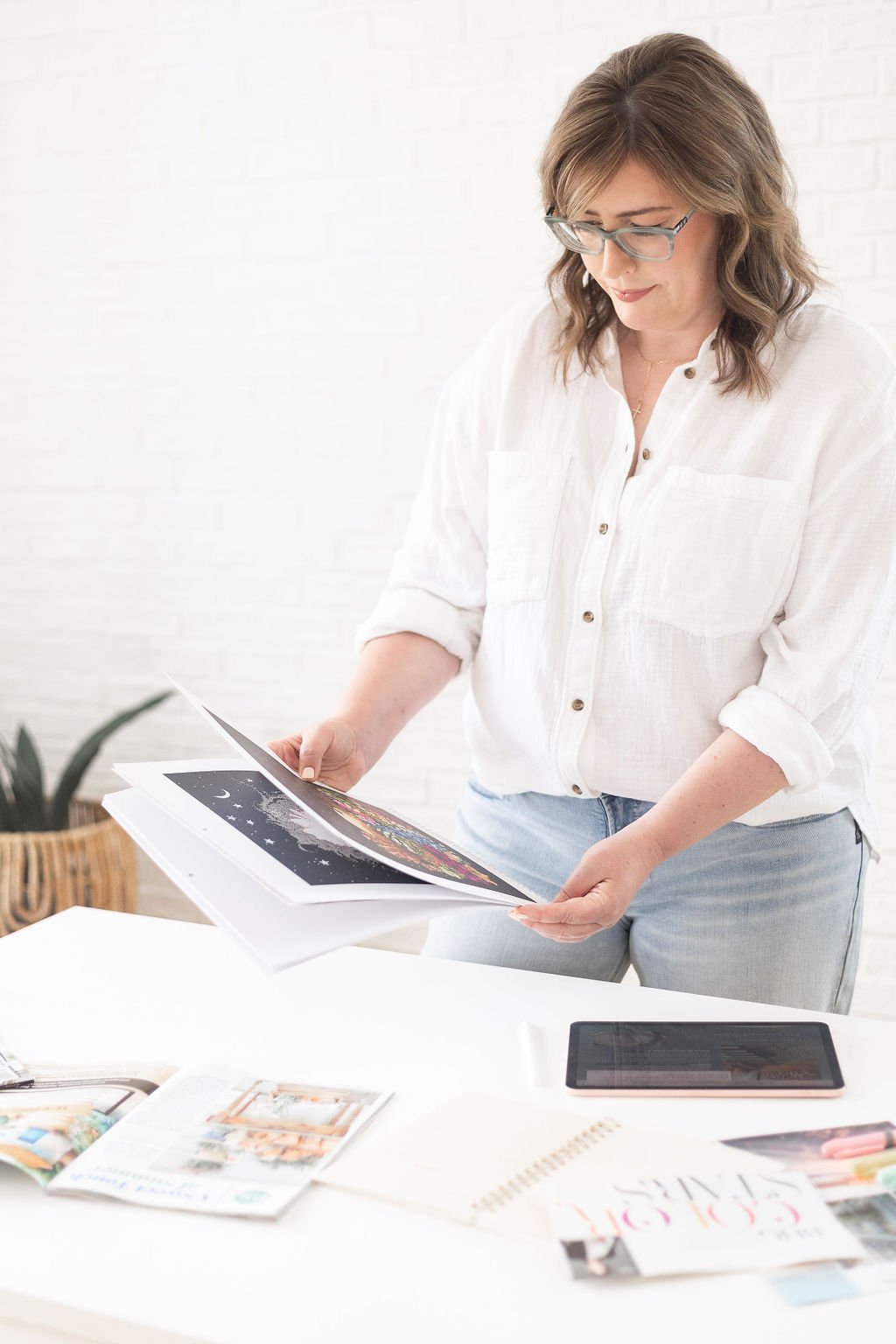 Woman with glasses flipping through colorful art prints on a table.