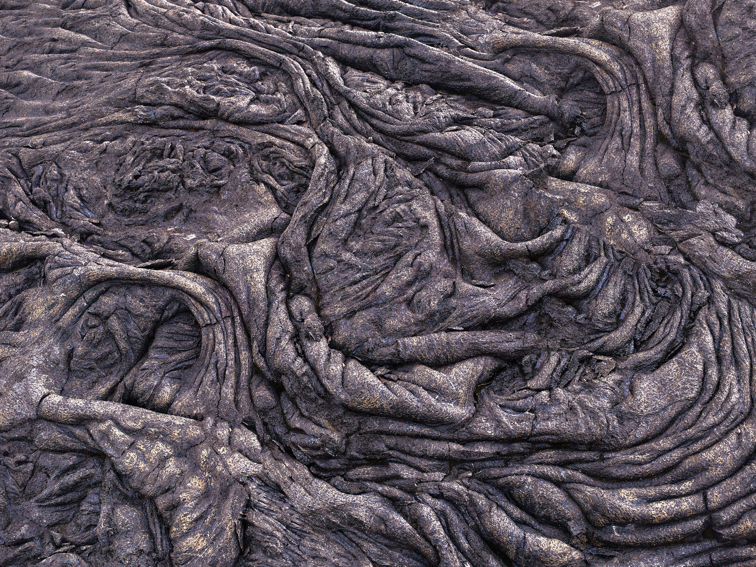 Close-up photo of twisted, dark volcanic rock formations with rough, layered textures.