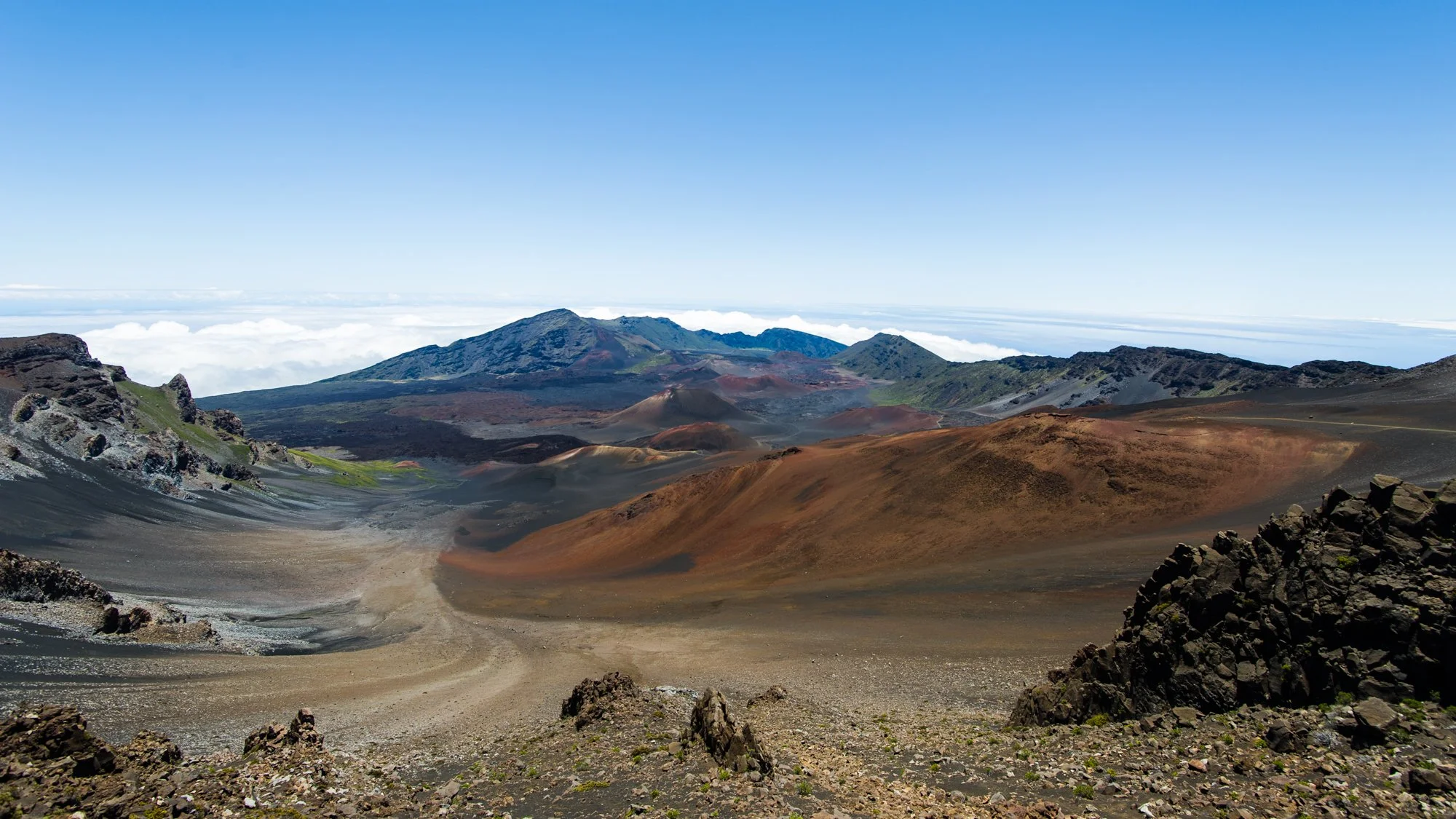 Volcanic landscape with multiple active volcanoes, rocky terrain, and a blue sky above.