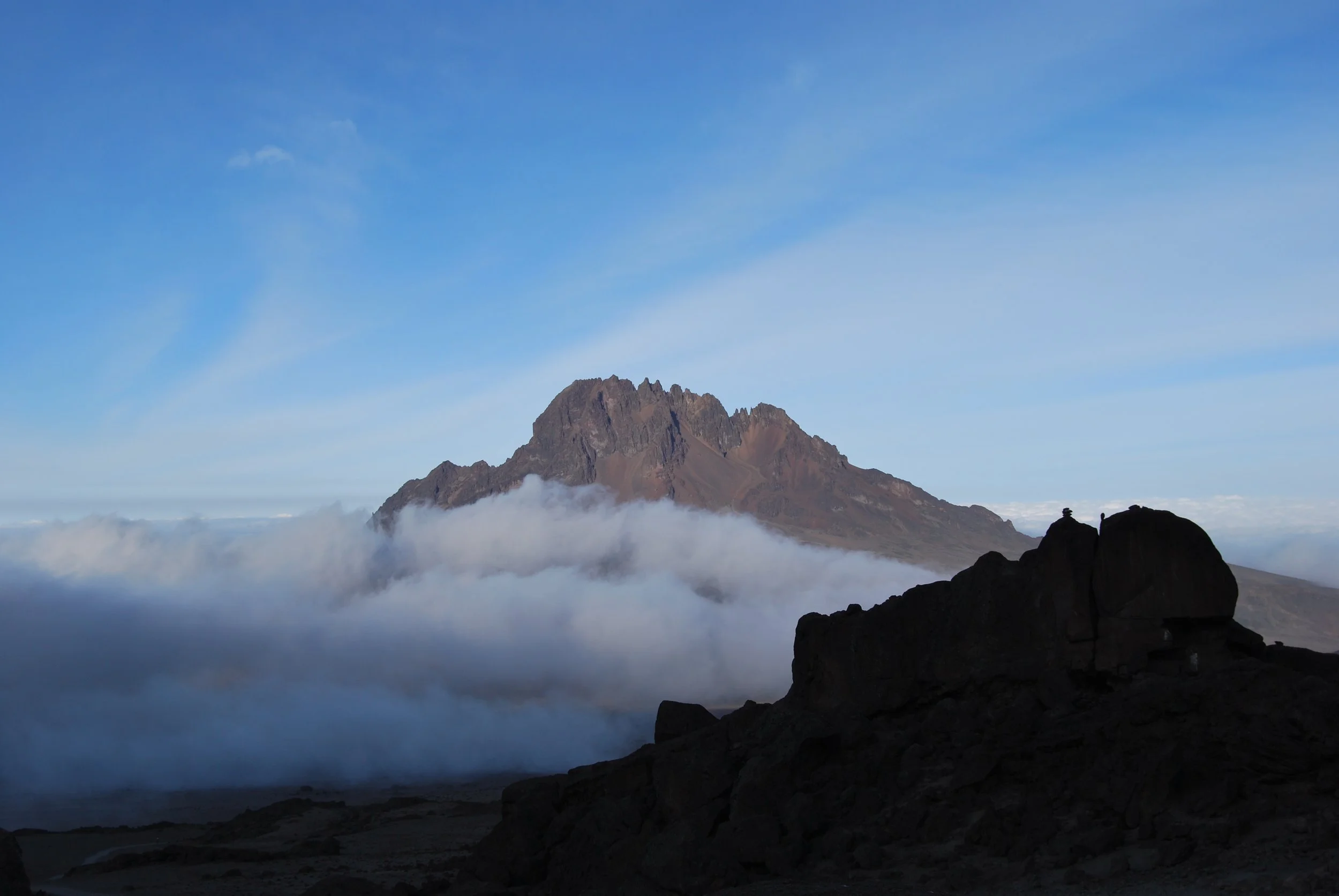 A mountain peak surrounded by clouds and a clear blue sky.
