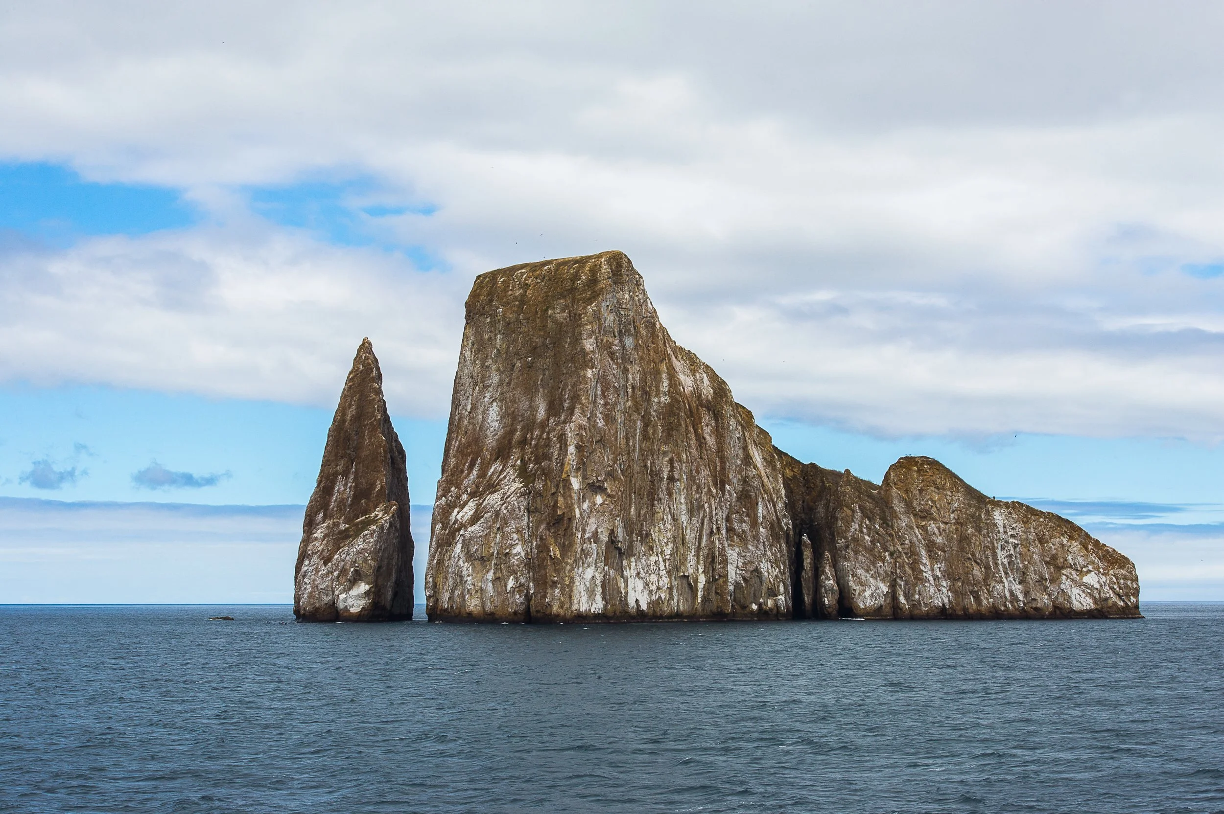Sea stacks rising from the ocean under a partly cloudy sky.
