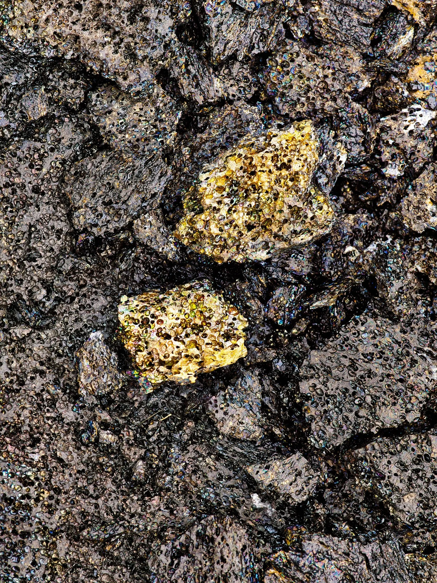 Close-up of volcanic rocks with shiny black and yellow mineral deposits.