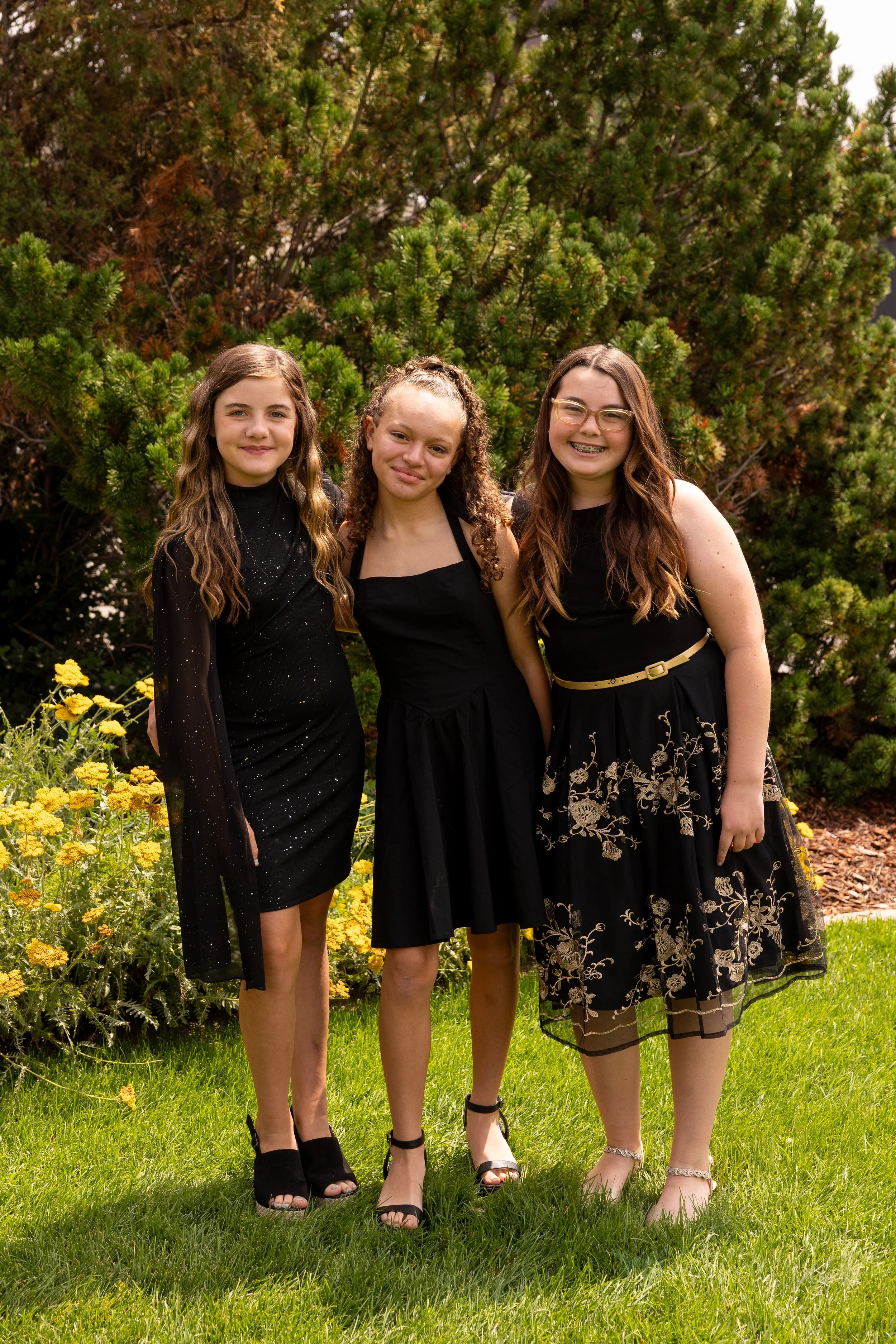 Three young girls dressed in black formal dresses posing together outdoors at the Boss Babe Academy celebration.