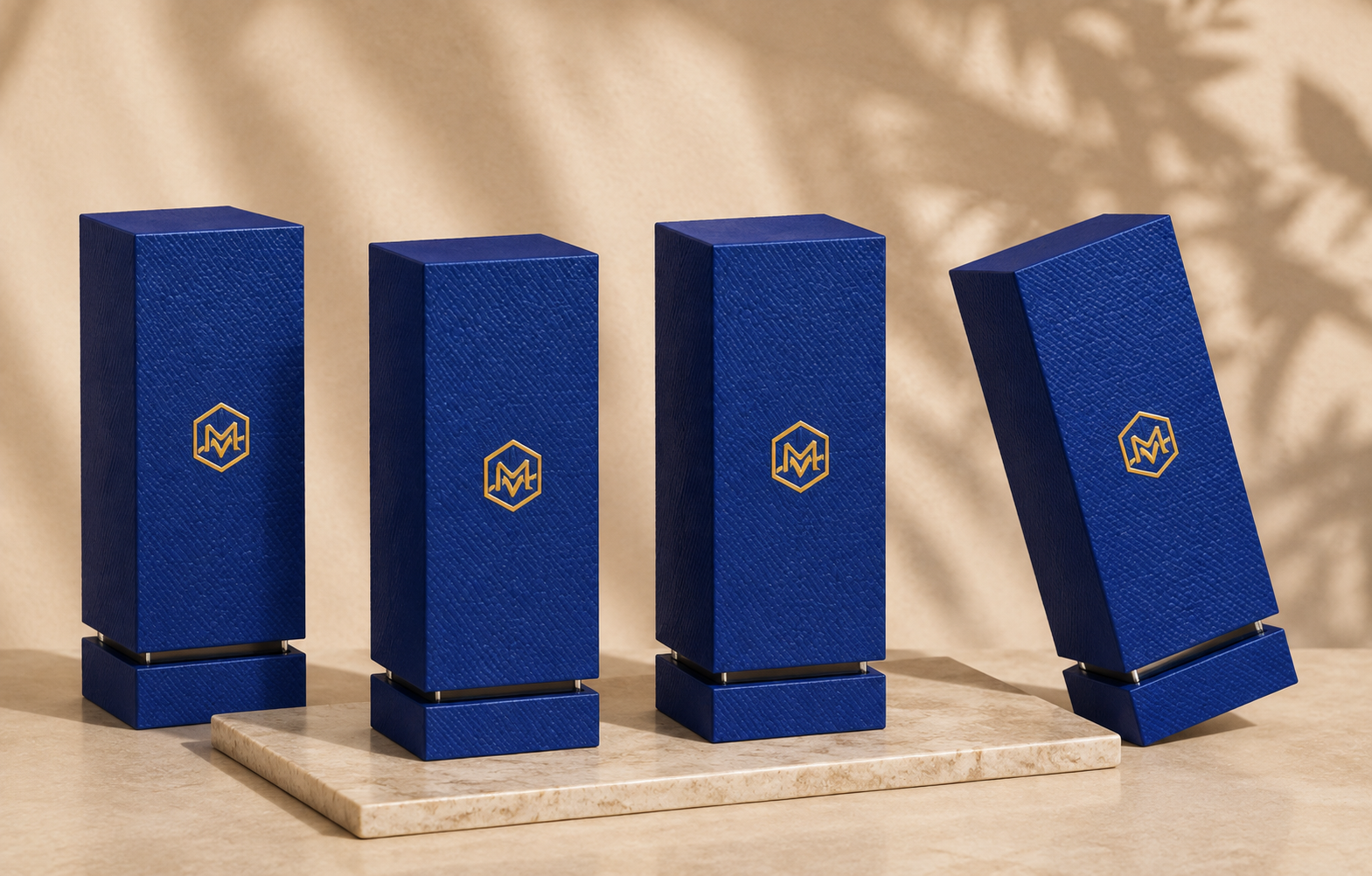 A row of four tall blue rectangular boxes with textured surfaces and gold logo, with one box tilted at an angle, placed on a marble platform on a beige surface, with shadows cast on a beige background.