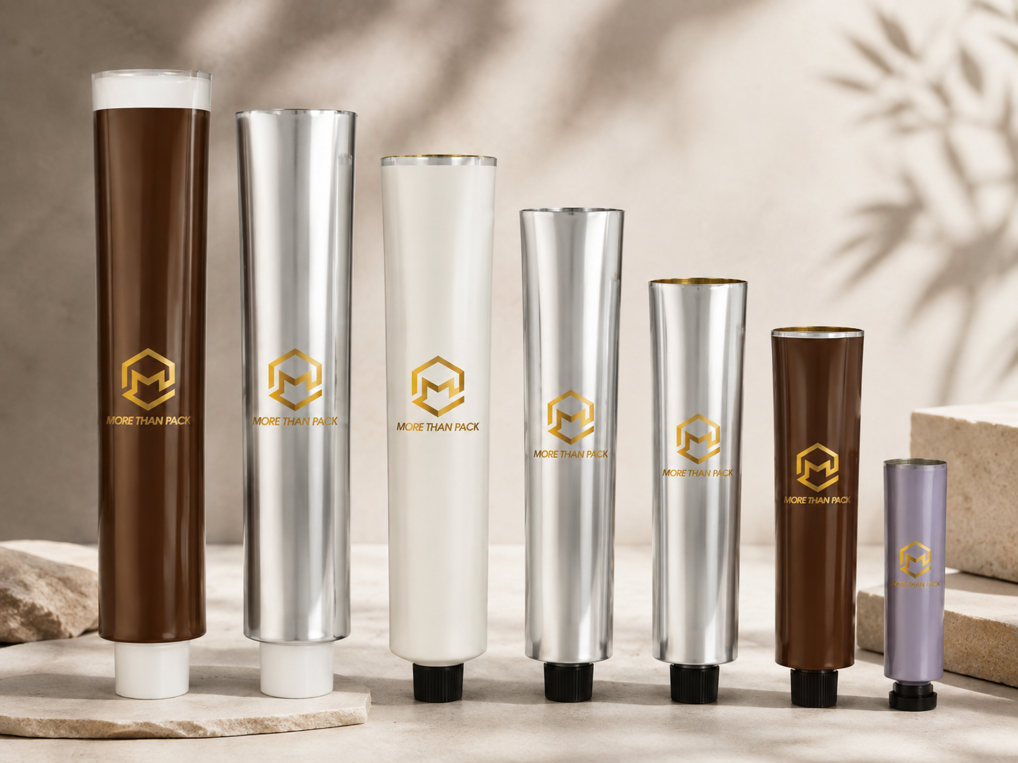 Assorted beauty or skincare product tubes with gold logo and text on a neutral background.