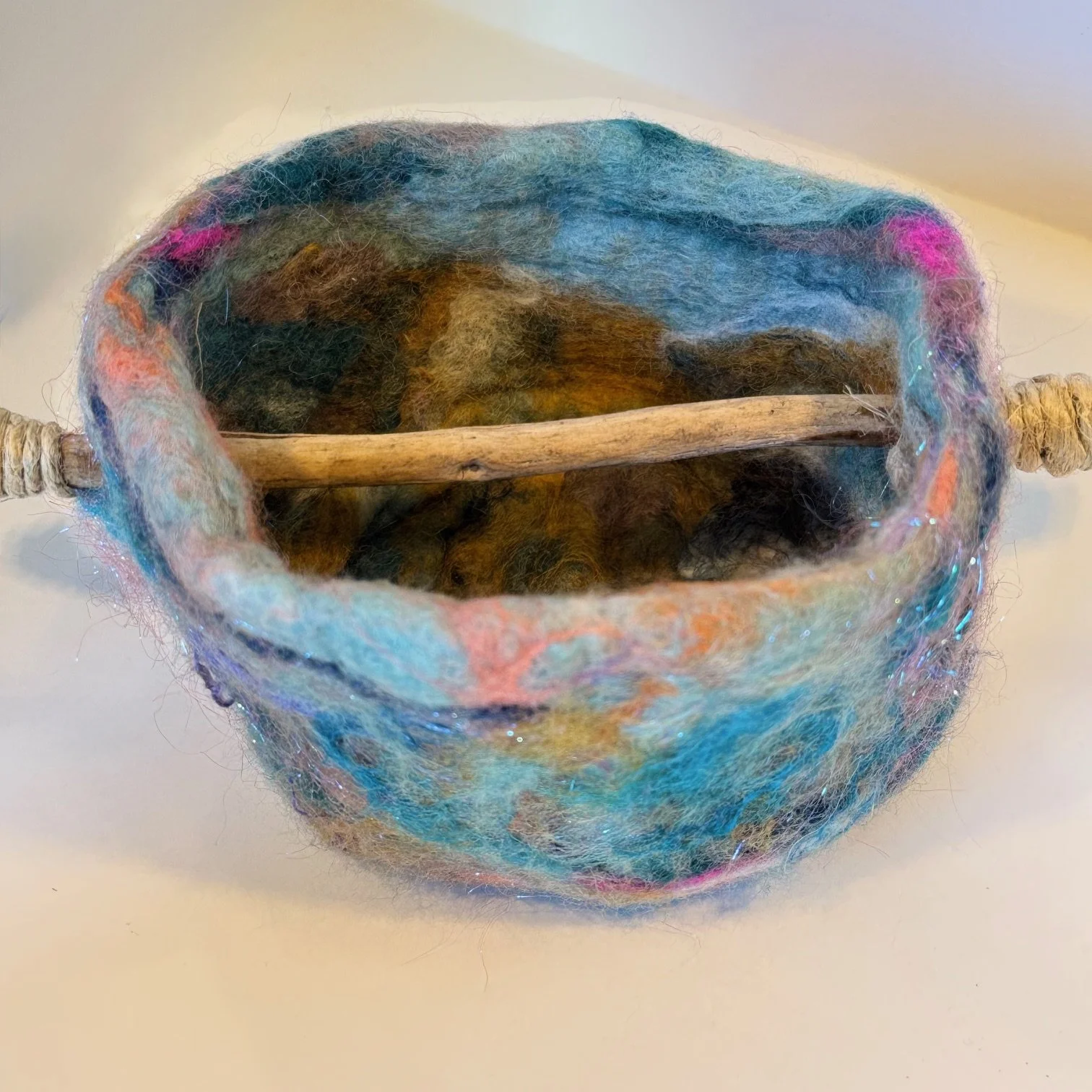 Wet felted wool roving with resist, organic silk fiber, and sheep locks into 4" round vessel with stick handle, 6/21/2025.