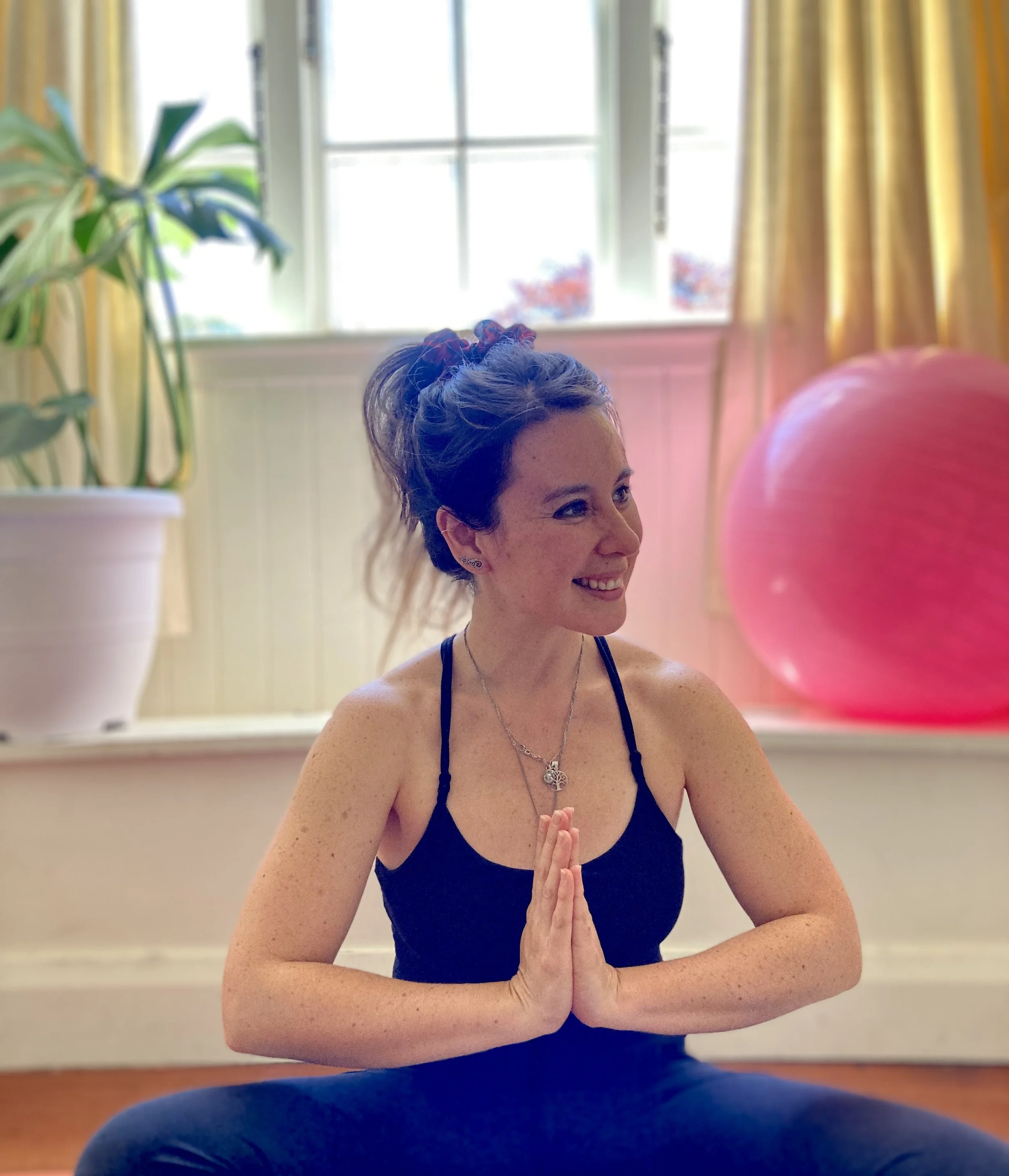 A portrait of Isidora Roa Yoga Teacher and Health Coach. Isidora is smiling at her small class (max 8 people). The class members are not visible.