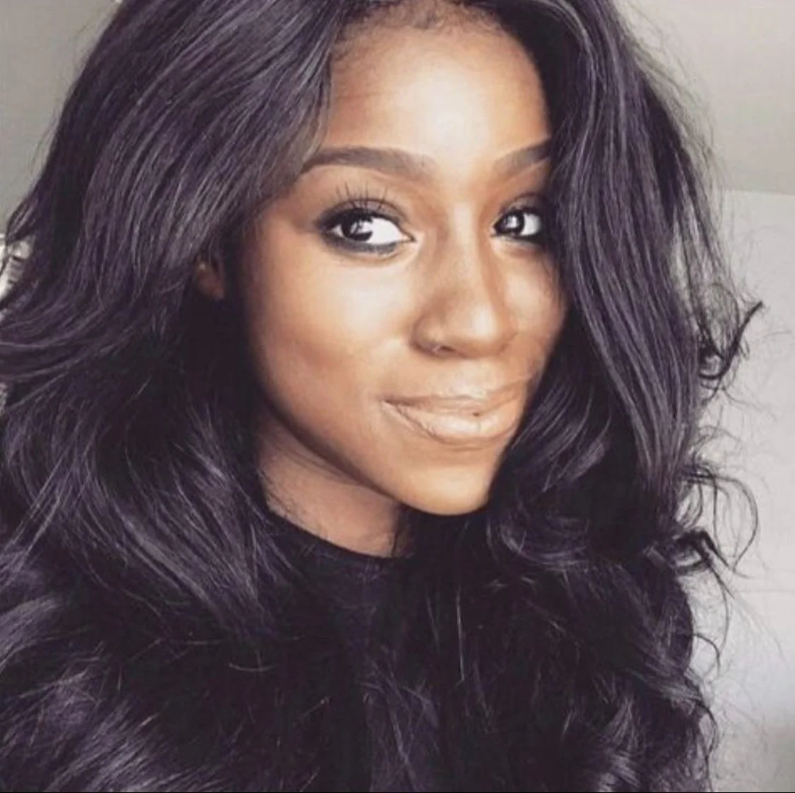 Close-up of a woman with long, wavy, dark purple hair and a subtle smile.