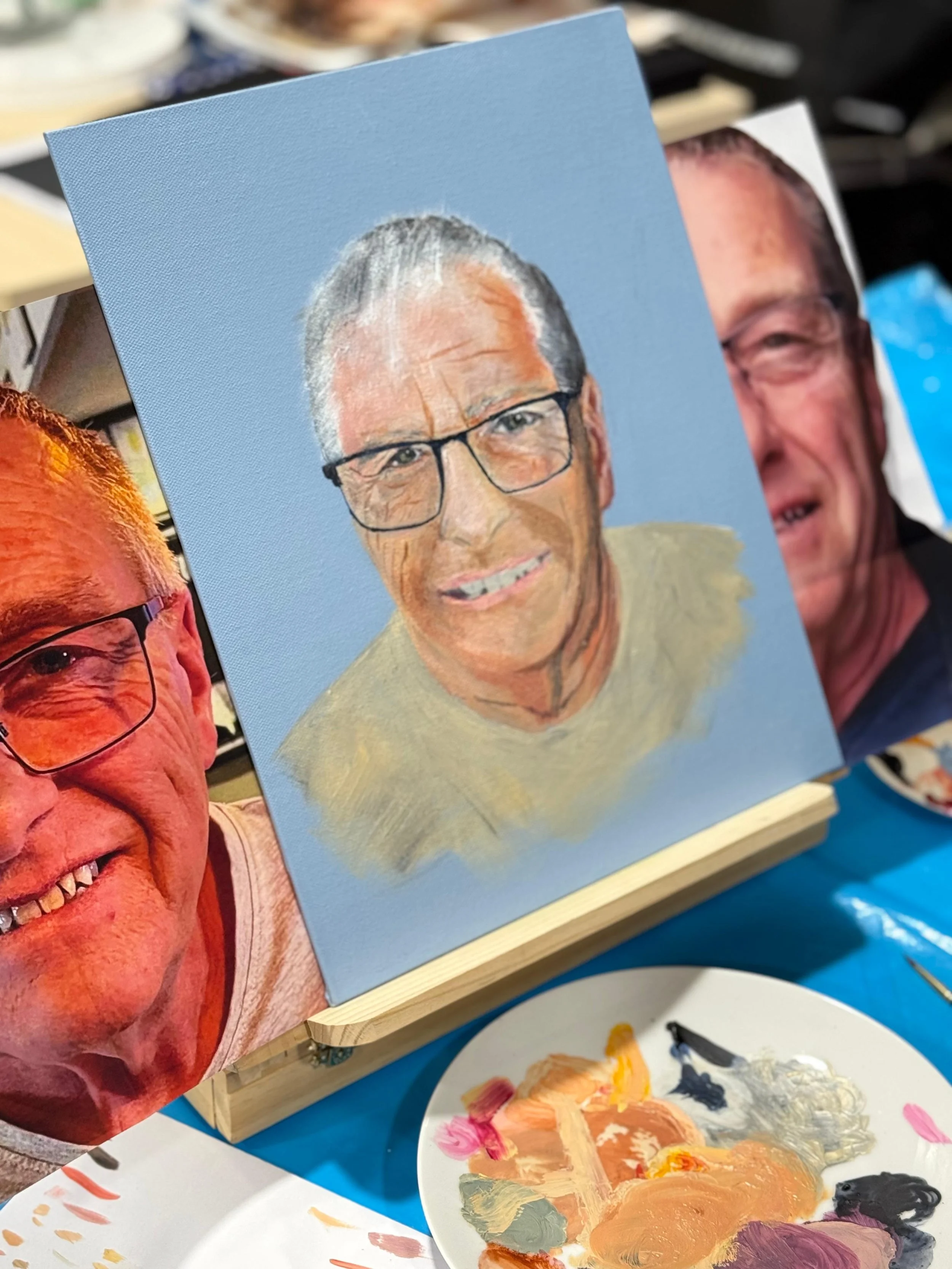 A group of women in a community center holding colorful abstract floral paintings, smiling and showing their artwork.
