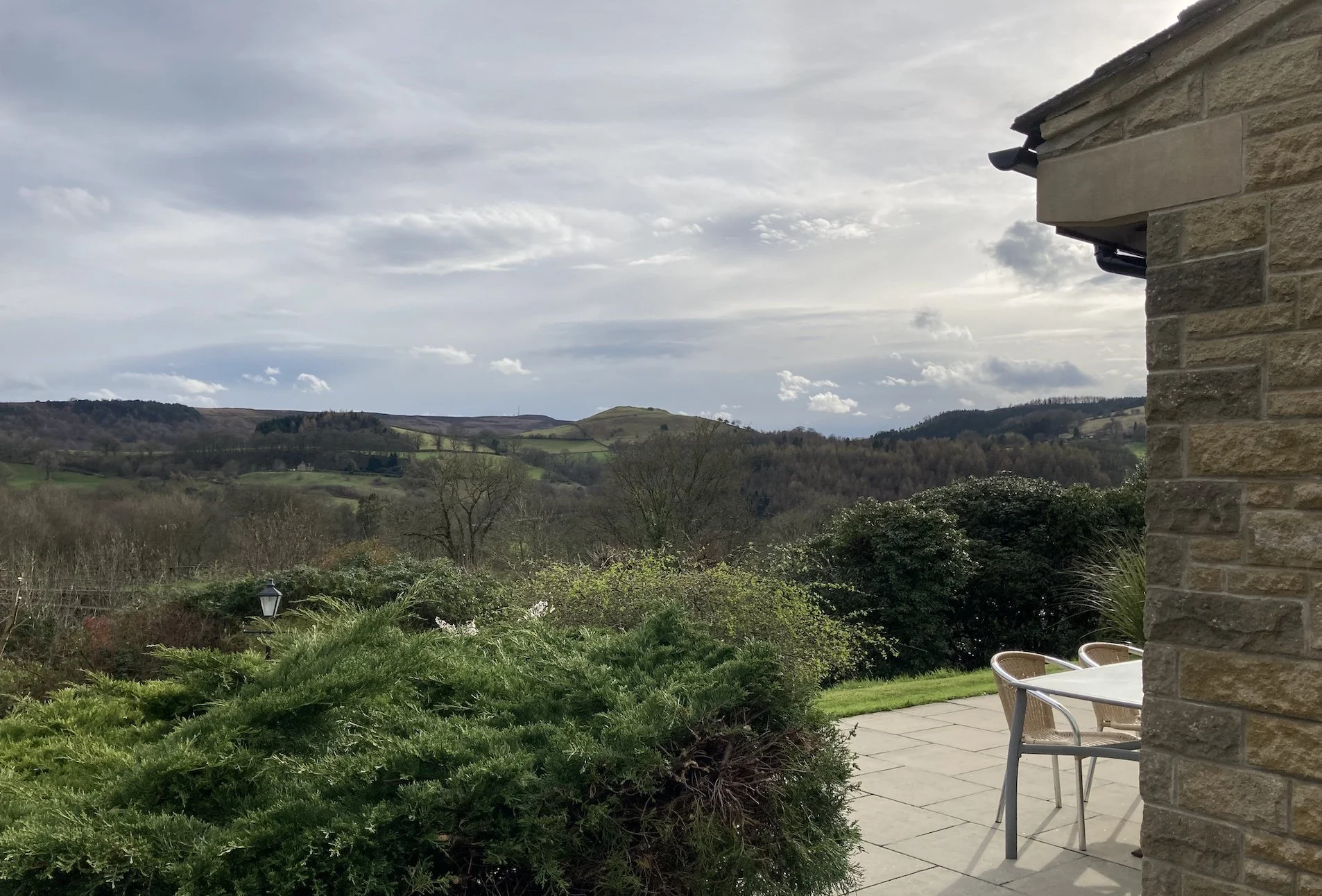 View from a patio with a round table and chairs, overlooking rolling hills and a cloudy sky.