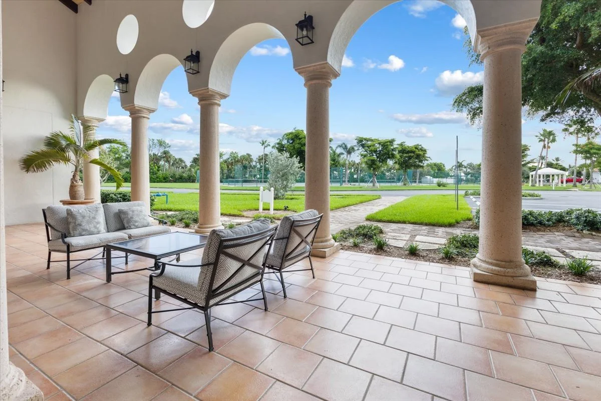 View of a covered patio with outdoor seating, columns, and a landscaped yard with trees and grass.