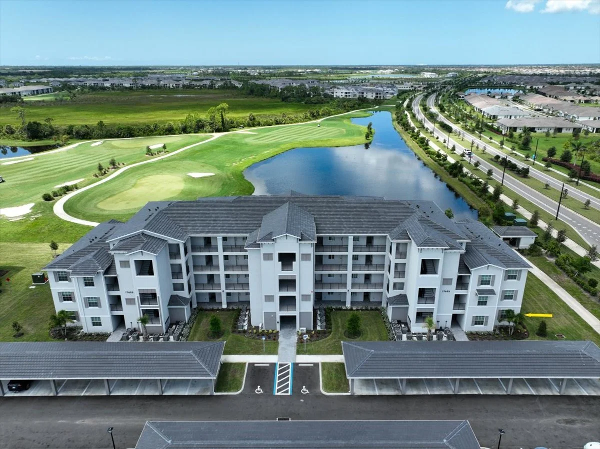 Aerial view of a modern residential apartment complex next to a golf course with a water body and surrounding green landscape.