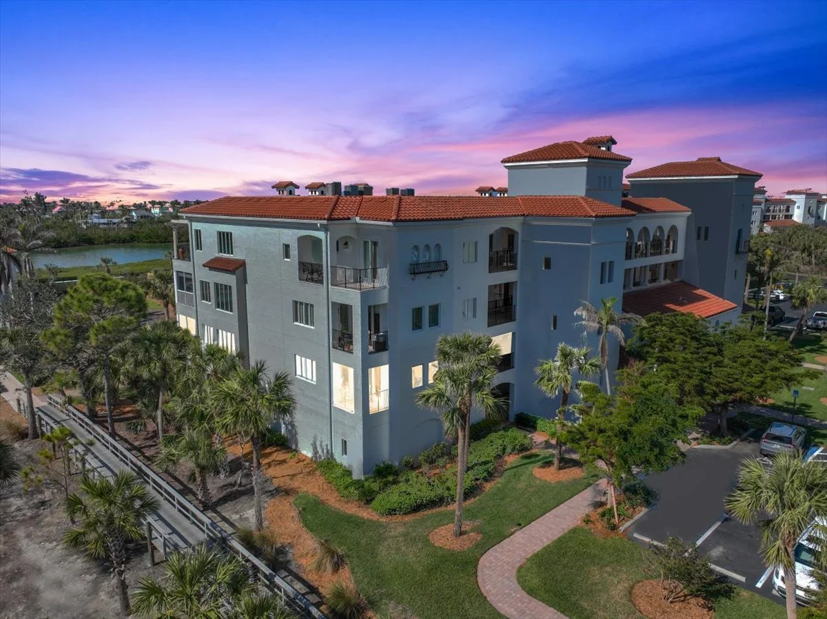 Multi-story residential building with red-tiled roof surrounded by palm trees and green landscaping during sunset.