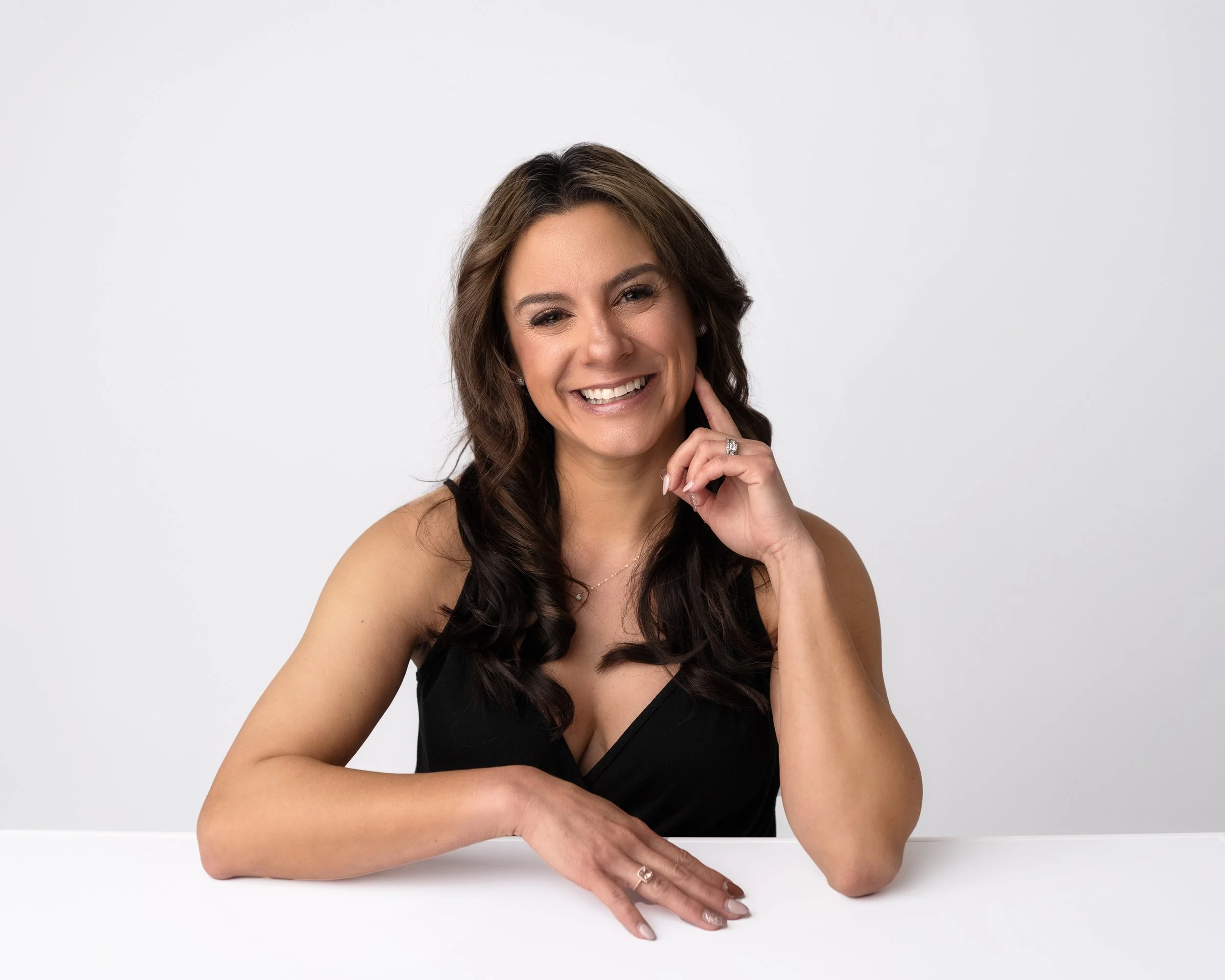 A family of four smiling and hugging outdoors in a park with trees, autumn leaves, and sunlight.
