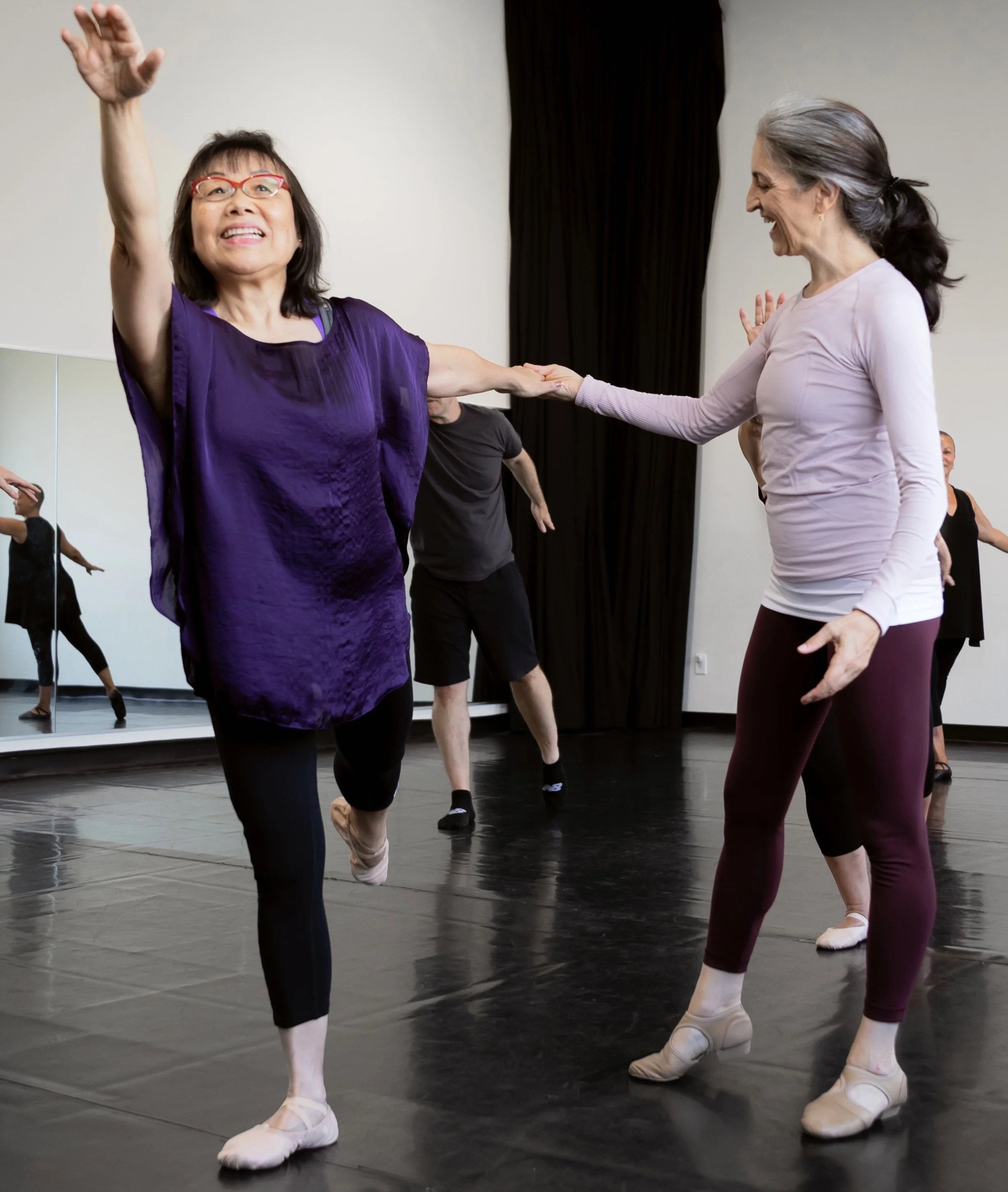 Image of ballet teacher helping adult student ballance on one leg with other lifted in straight line called an arabesque