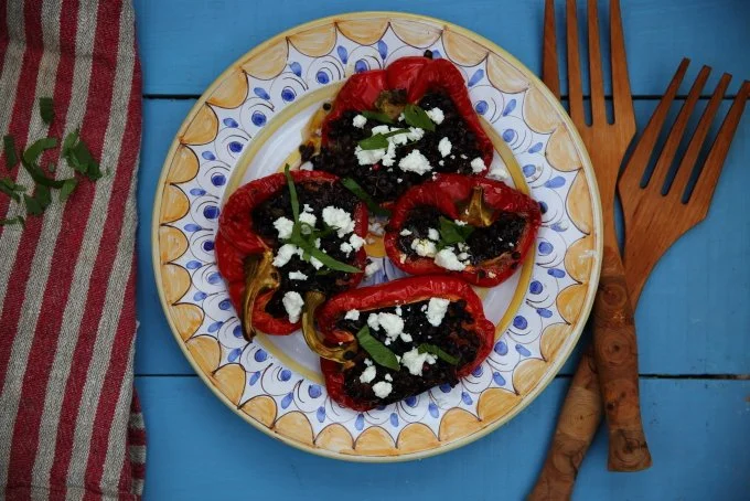 Roasted red bell peppers stuffed with black beans, topped with crumbled cheese and fresh basil leaves, served on a decorative plate.