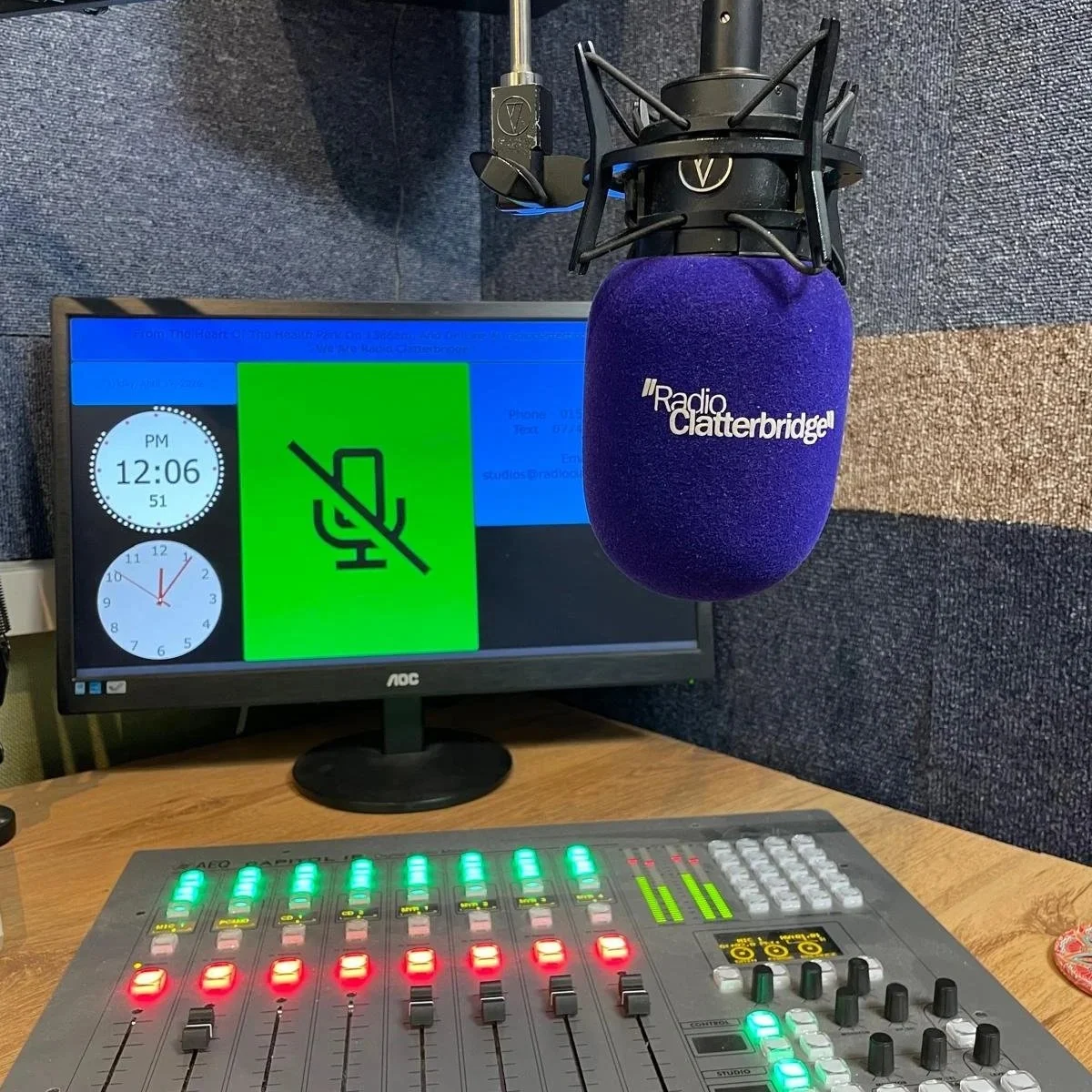 Recording studio with a microphone labeled Radio Clatterbridge, a computer monitor displaying a muted audio icon, clock, and email info, and a sound mixing console with illuminated faders.