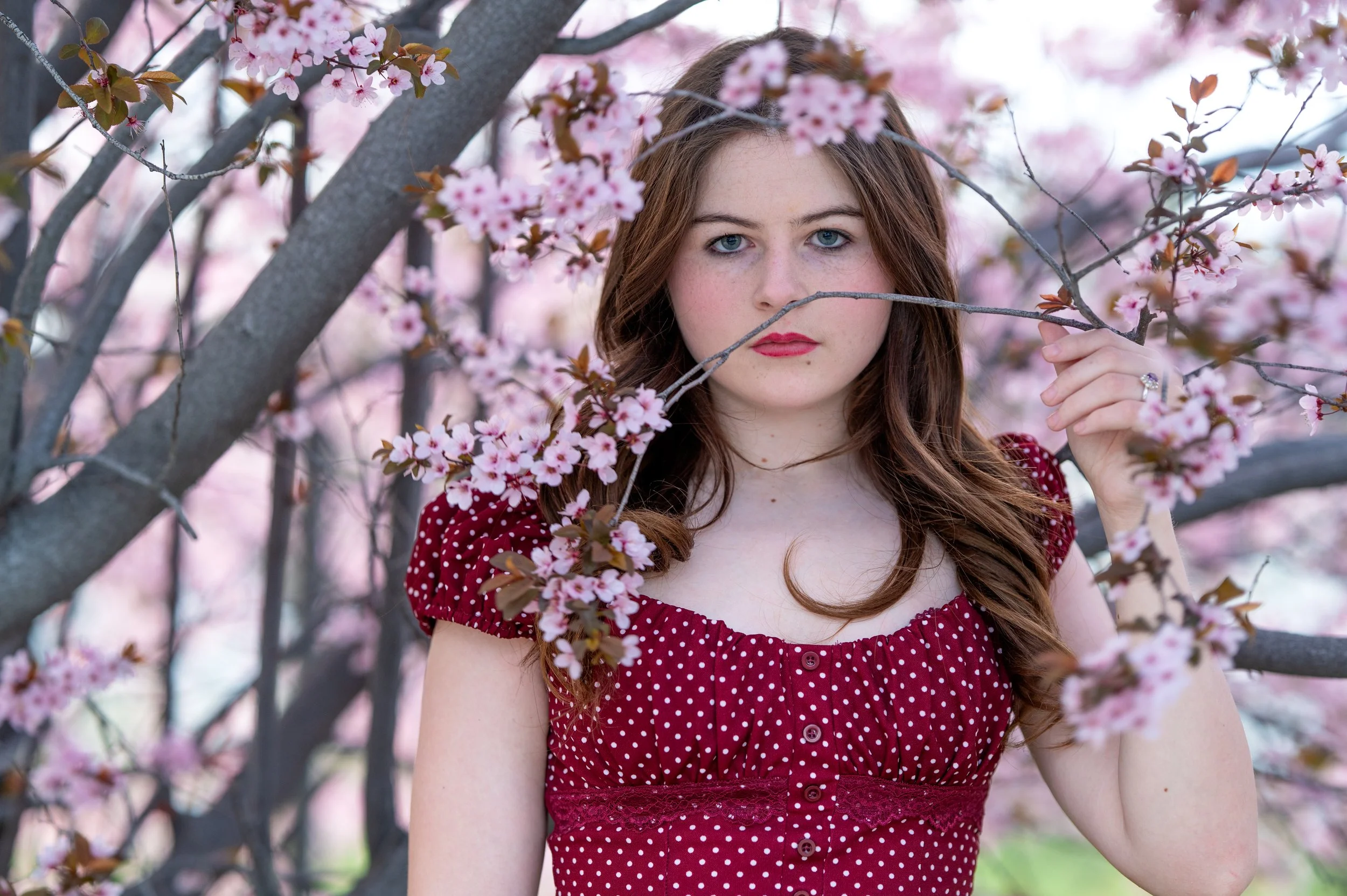 18 year old girl peeking through the blossoms on a branch of a flowering tree.