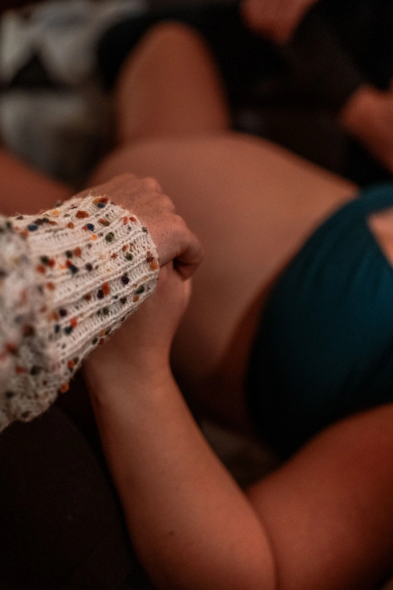 Birth Photography: A woman labors while lying on a rug holding hands with a certified doula Nina Koehler.