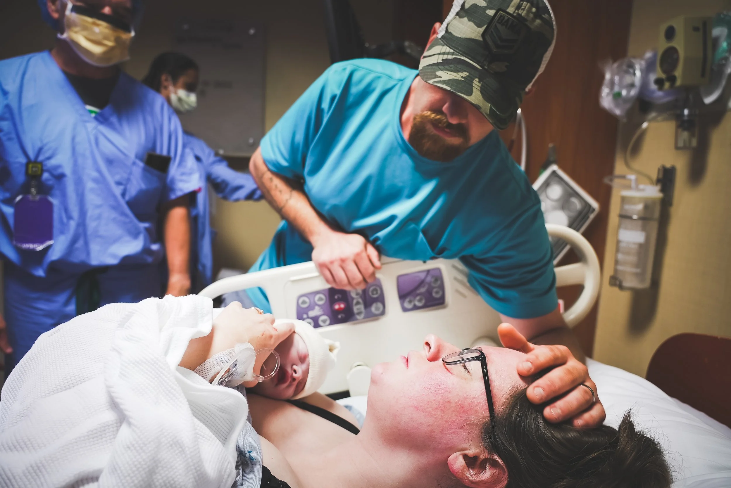 Birth Photography: Healthcare workers in a hospital room assisting a woman in labor, with a newborn baby resting on her chest.