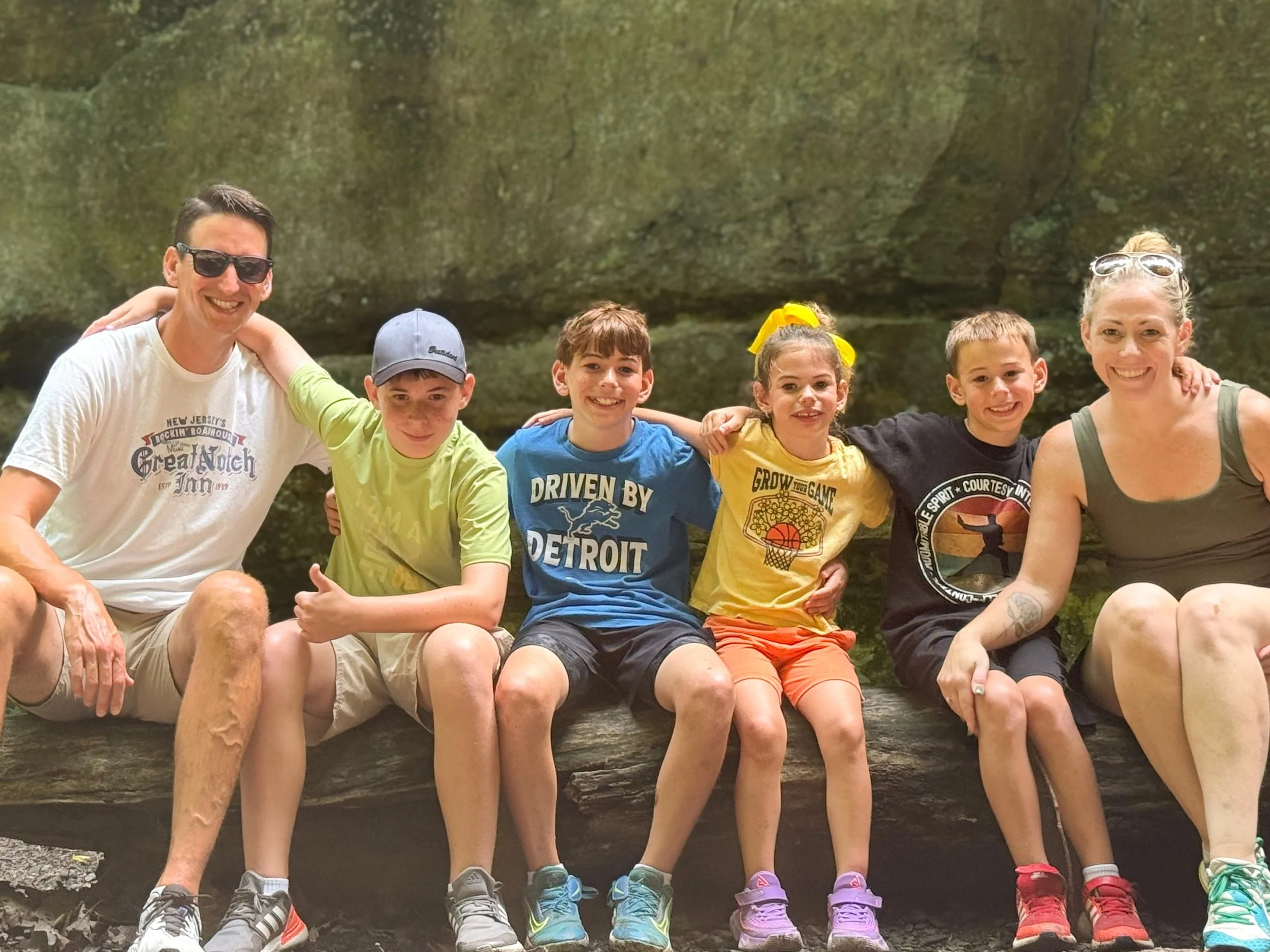 Certified Doula and photographer/videographer Nina Koehler and her family sitting on a log outdoors with a rocky background, smiling for a photo.