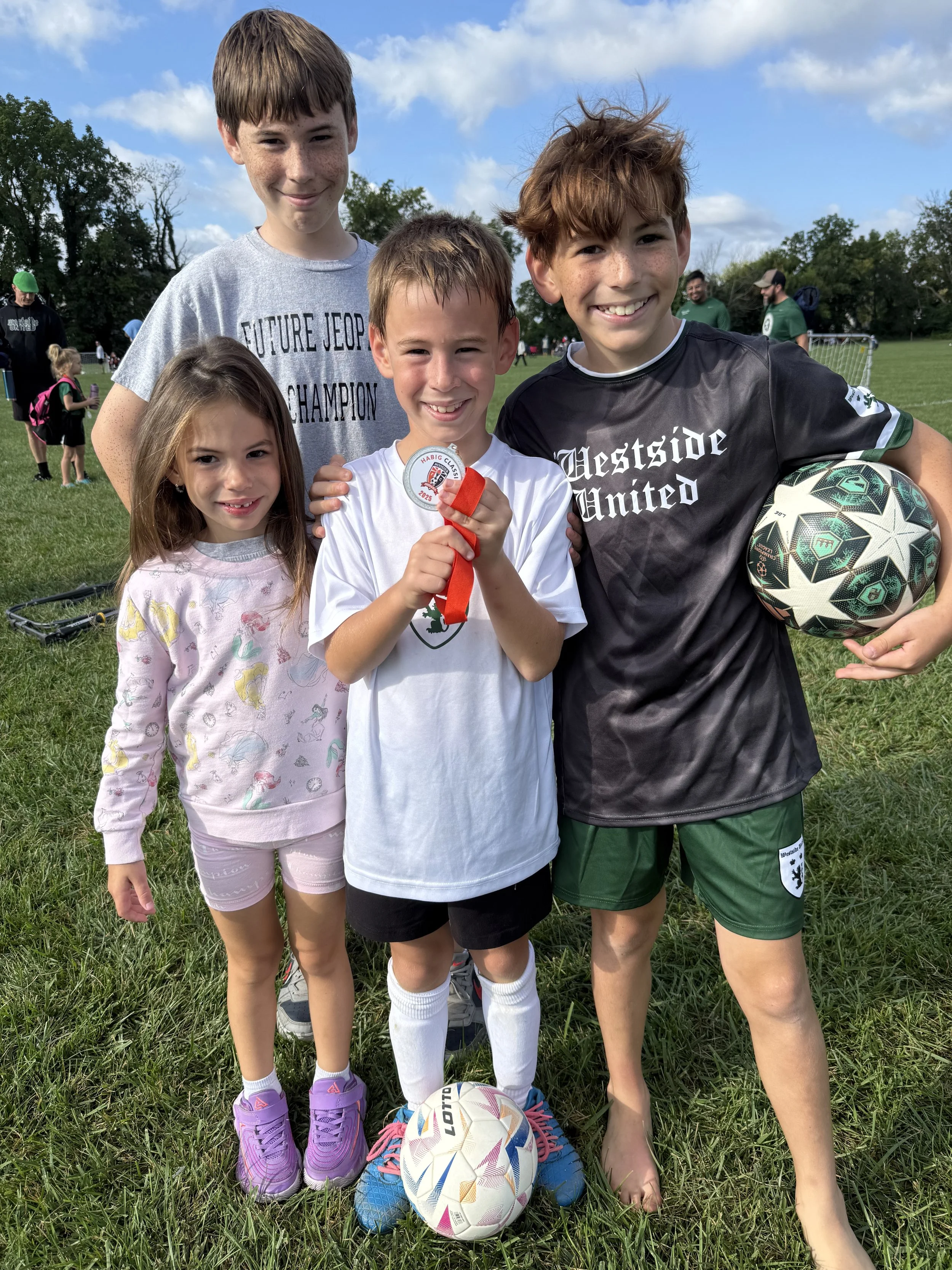 Certified Doula and photographer/videographer Nina Koehler kids on a soccer field, celebrating a youth soccer game, with some holding a soccer ball and a medal.