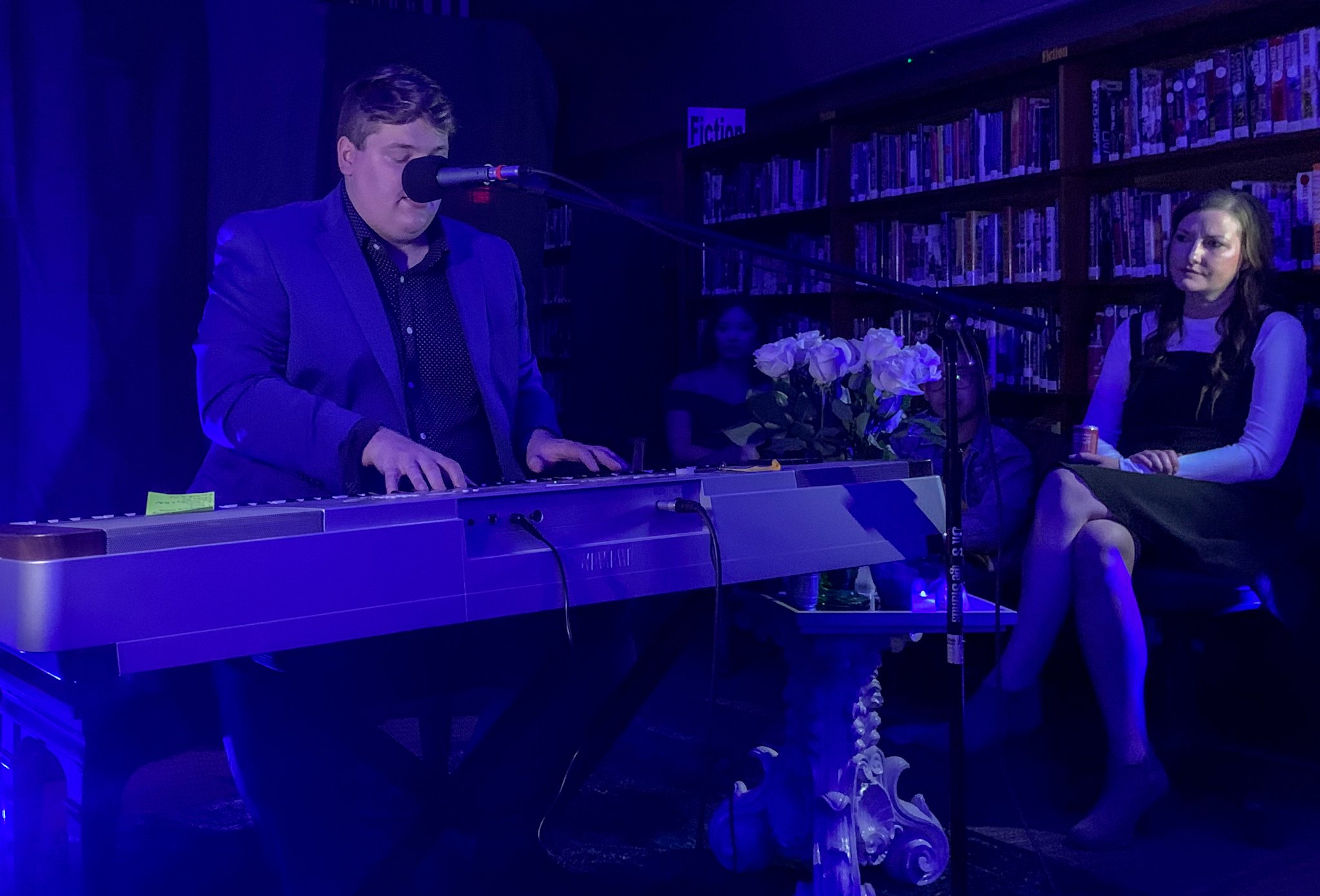 Alex performs at the piano while a friend listens