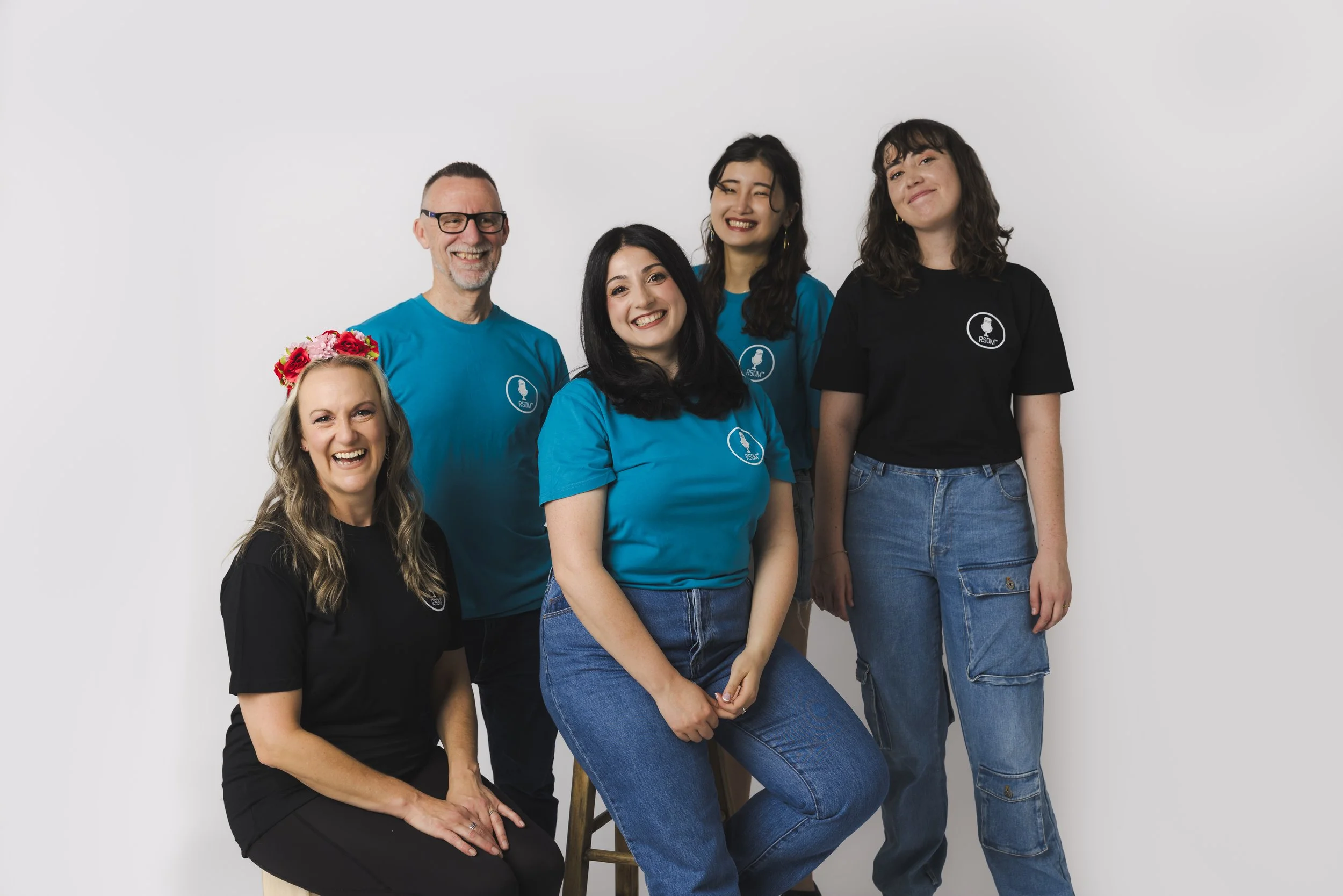 Group of five smiling people, four women and one man, wearing casual clothing with matching logo, posing against a plain white background.