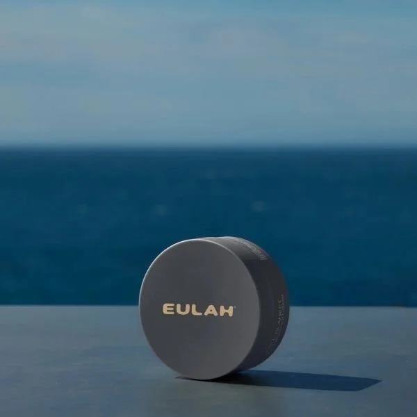 A round pot of Eulah skincare in front of the sea