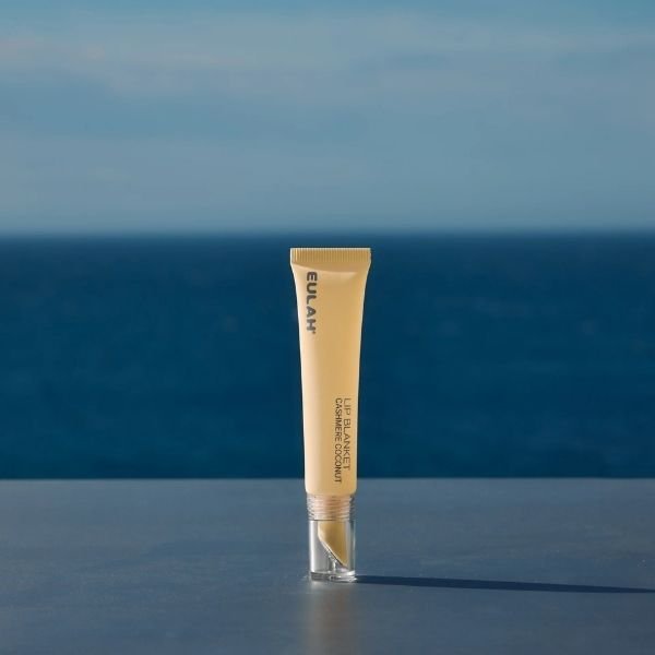 A lip product in a yellow tube against a blue sea