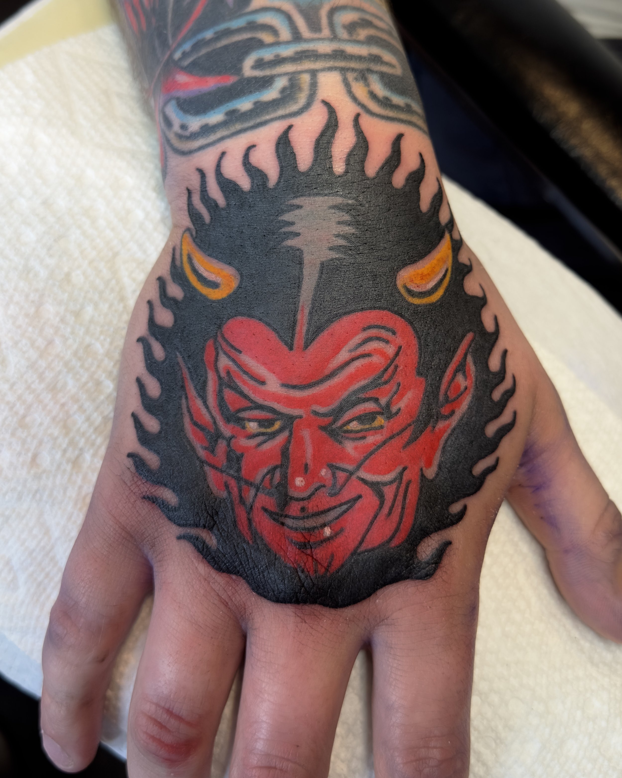 Color tattoo of a red devil face on a person's finger.