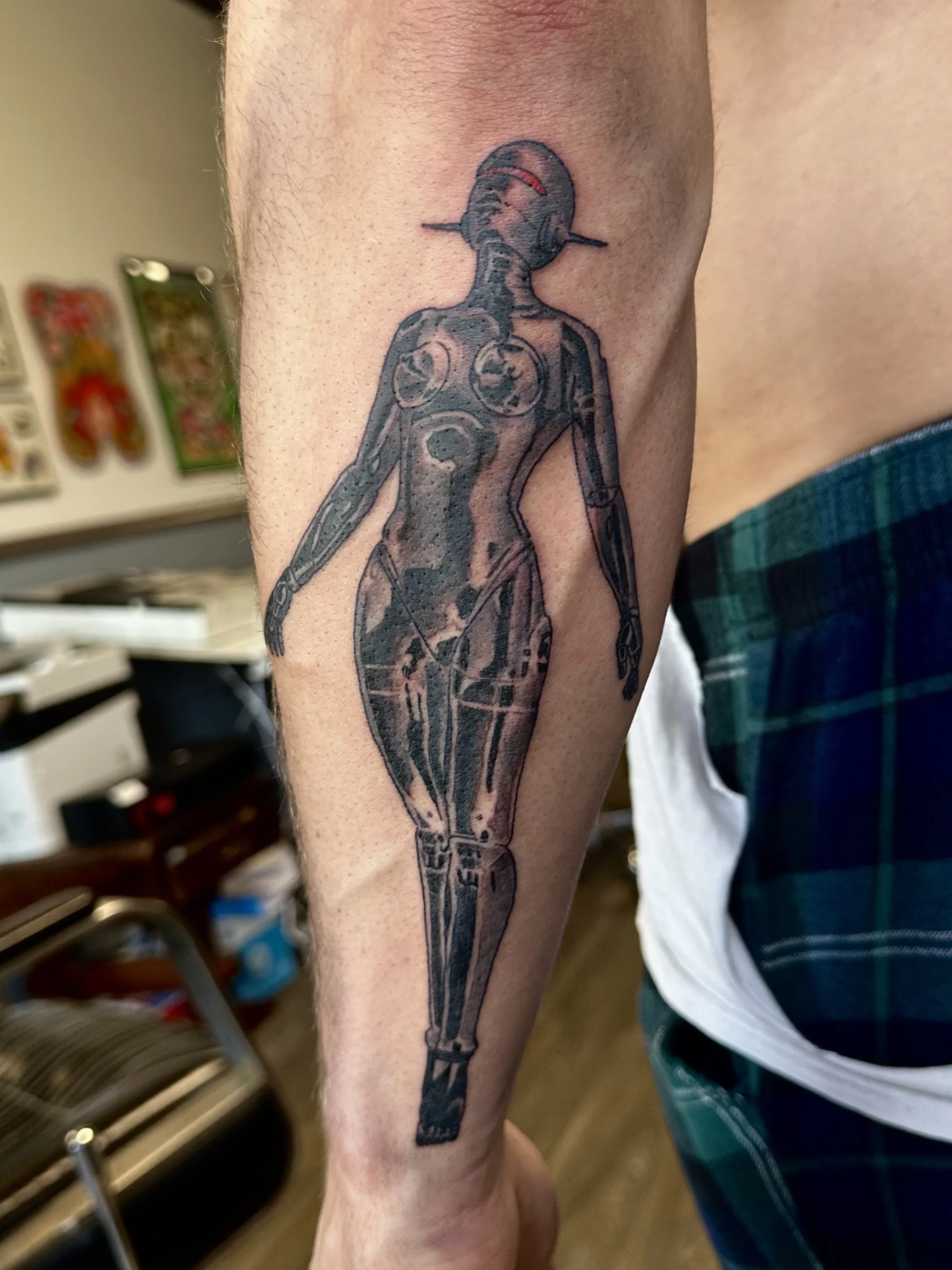 Tattoo of a robot with a human head, arms, and legs, holding a sword, located on a person's arm.