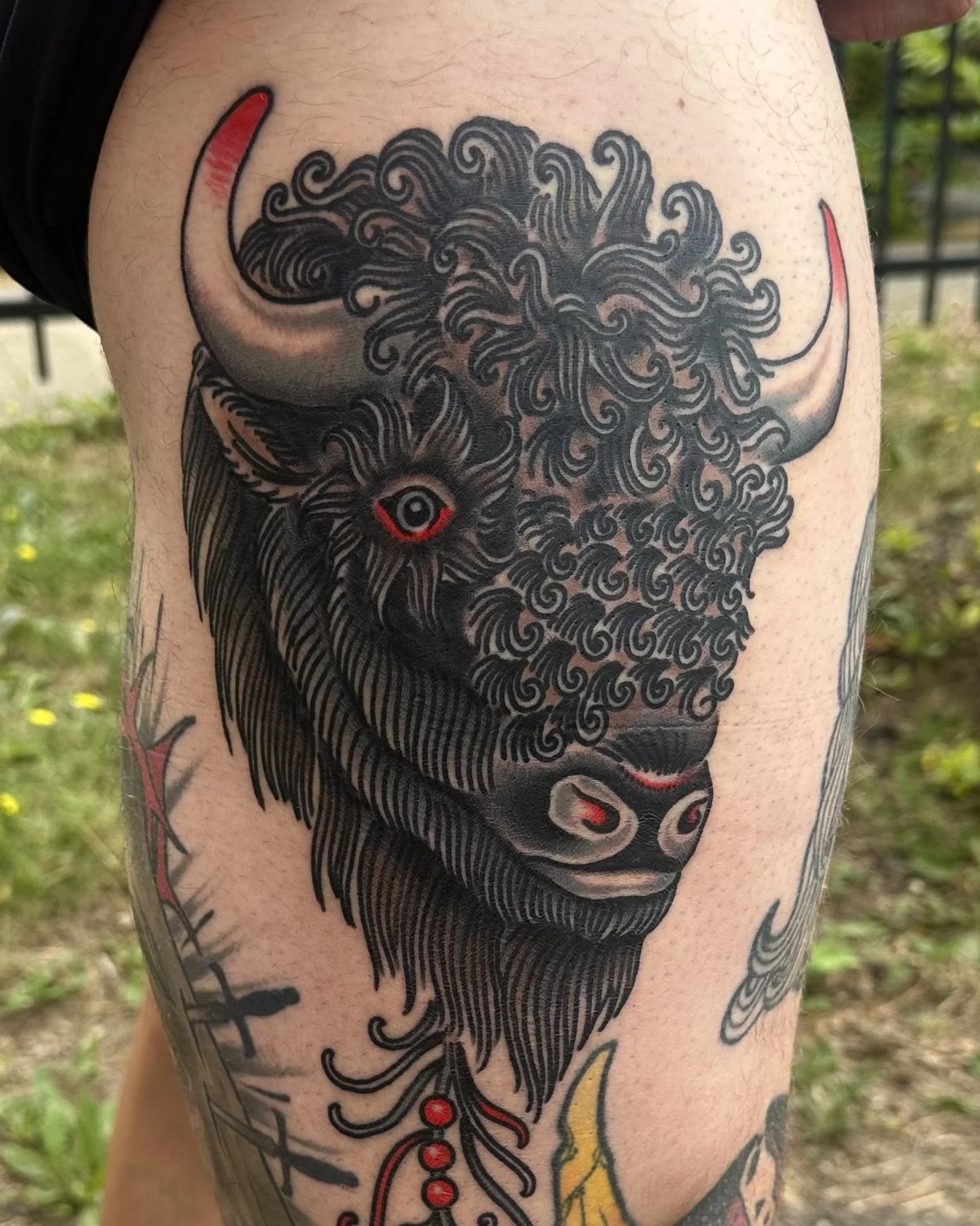 Tattoo of a stylized, curly-haired bull's head with red accents on its horns and eyes.