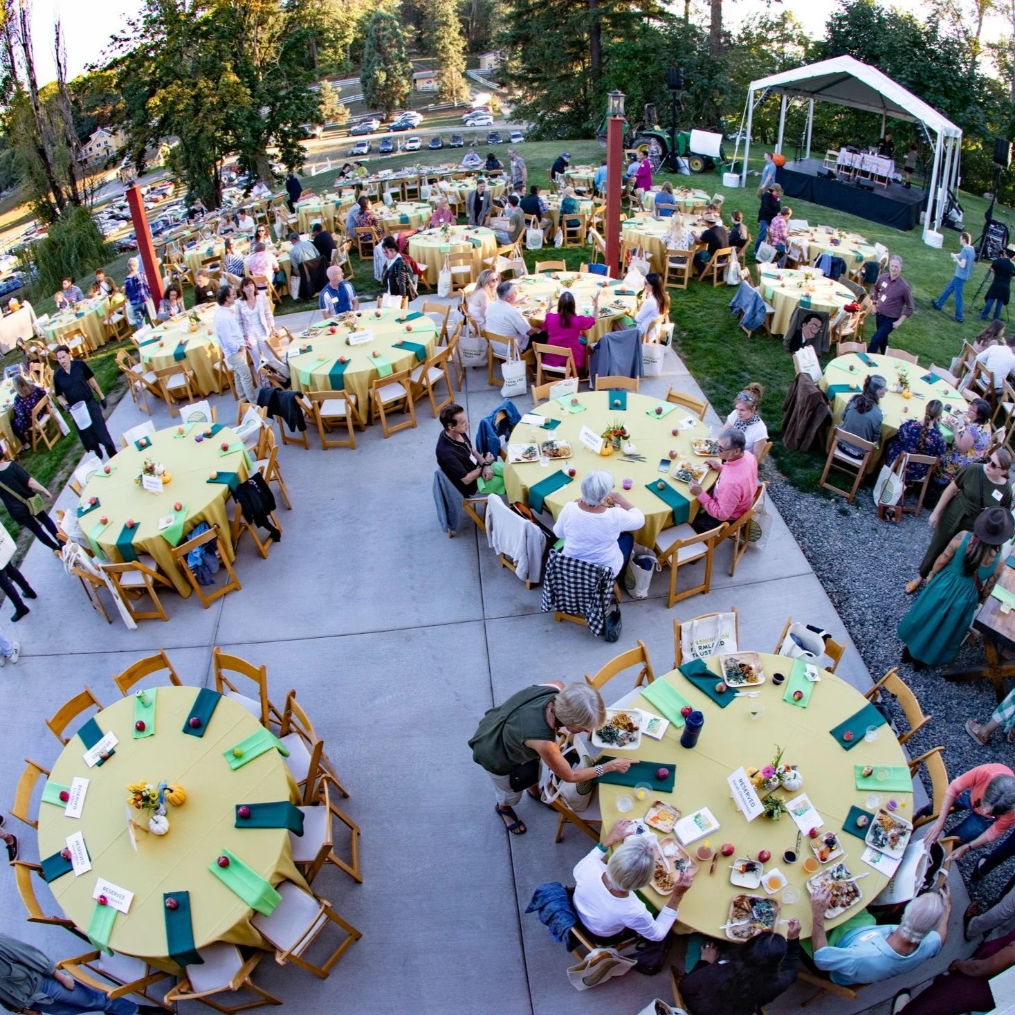 A bird's eye view of round tables in yellow table cloths in an outdoor garden space at an event.