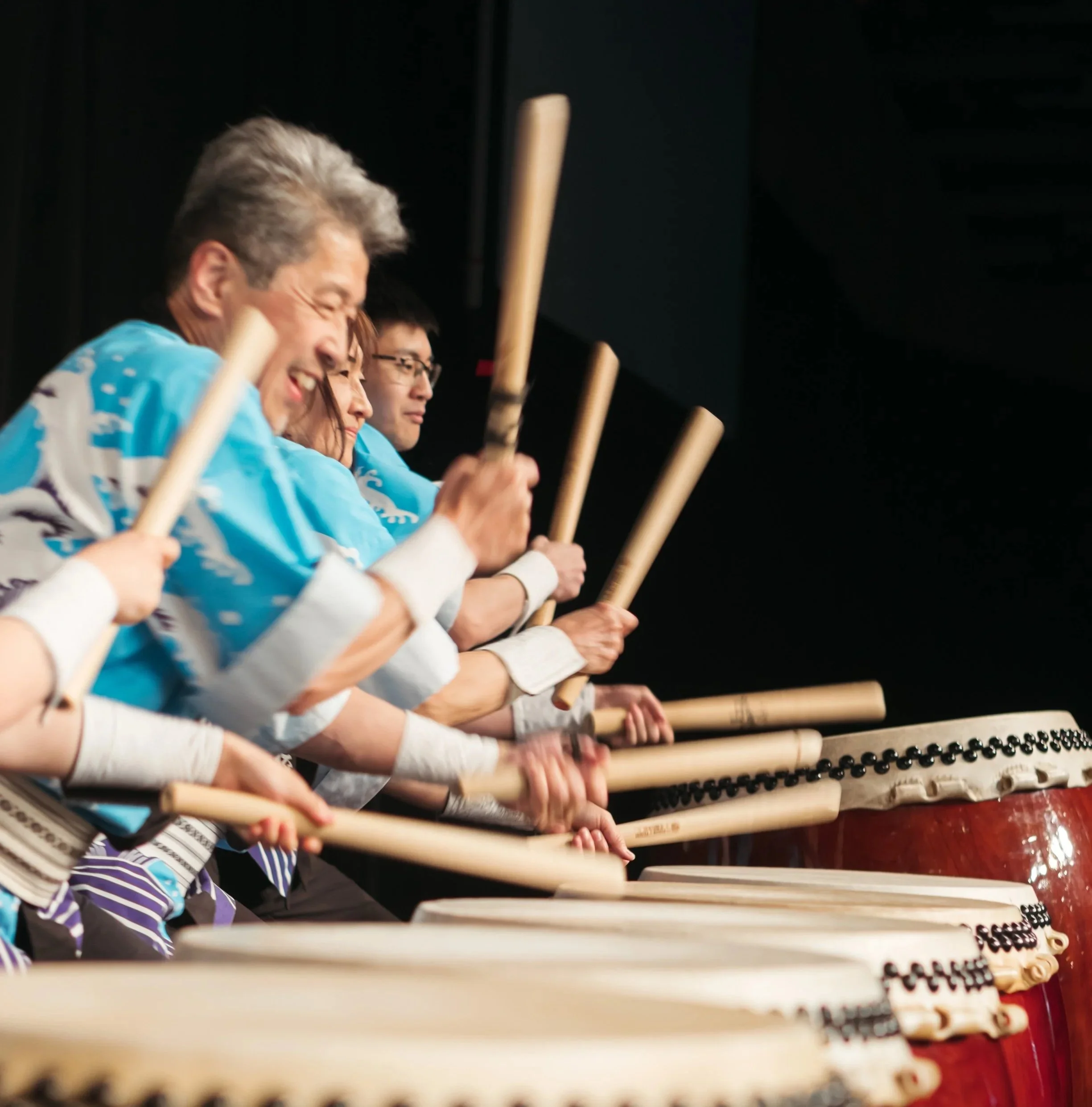 A row of performers handling wooden drumsticks.